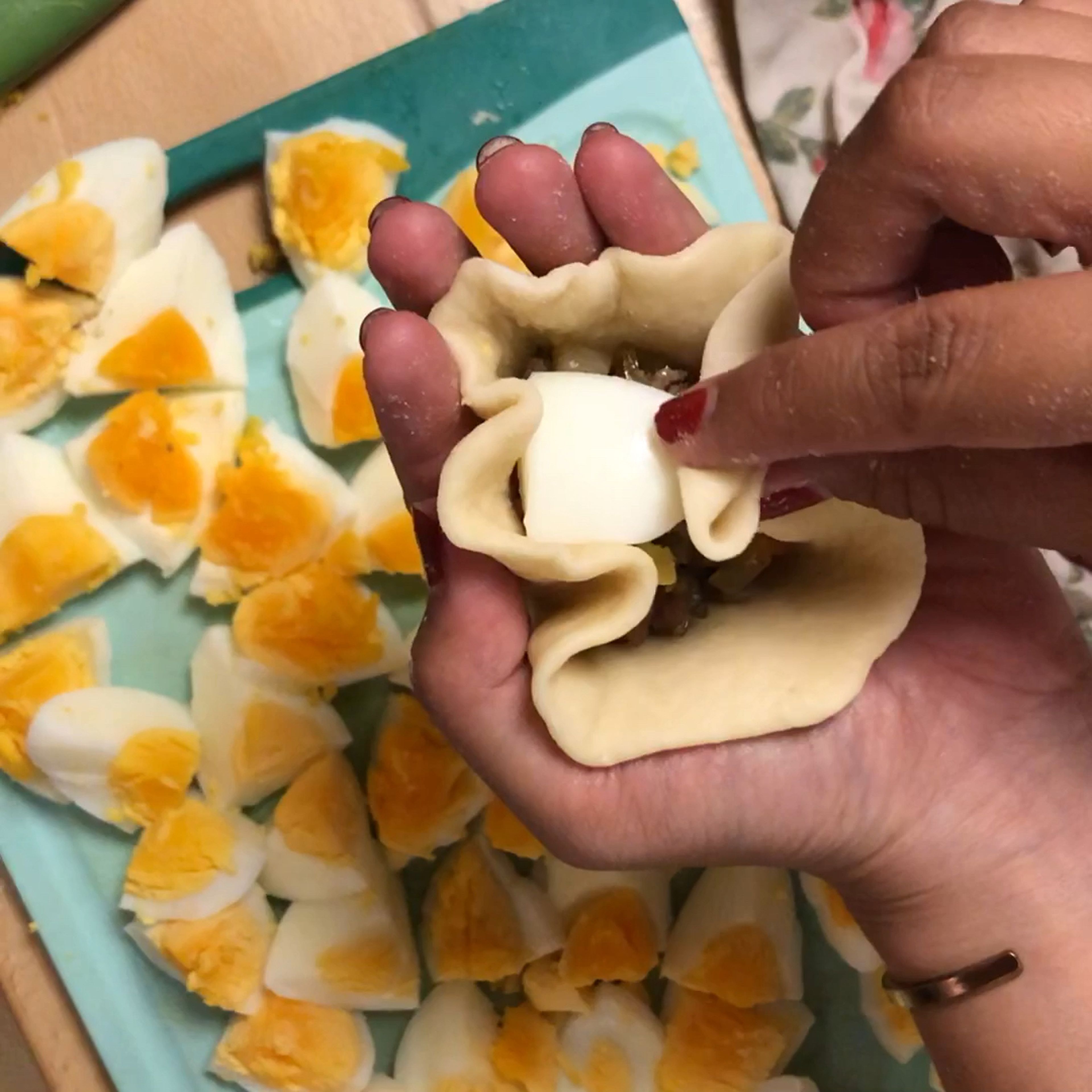 Backpapier in quadratische Stücke mit ca. 5cm Länge schneiden. Teig auf eine bemehlte Fläche geben und in 20 Stücke teilen. Diese mit einem feuchten Tuch bedecken. Ein Teigstück nehmen und zu einem Kreis (ca. 5-6cm Durchmesser) ausrollen. Teig auf die Handfläche legen und 3-4 EL Füllung in die Mitte geben. Ein halbes Ei drauf legen. Die Ränder vorsichtig hochziehen und fest zusammen drücken. Die Bao jeweils auf ein Stück Backpapier tun und mit einem feuchten Tuch bedecken.