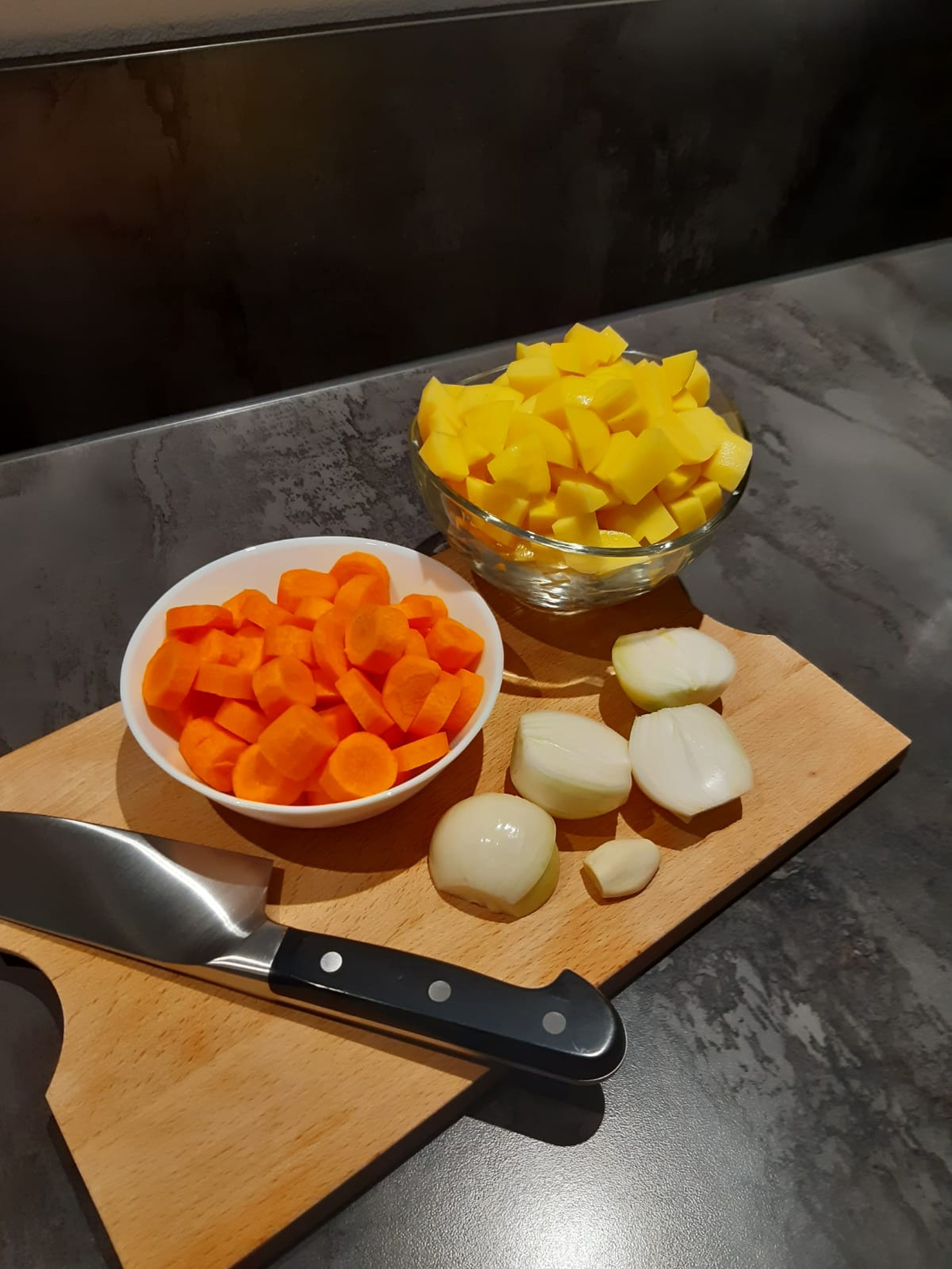 Zwiebeln, Knoblauch, Karotten und Kartoffeln schälen. Die Zwiebeln halbieren und die Kartoffeln und Karotten in 1 cm große Stücke schneiden