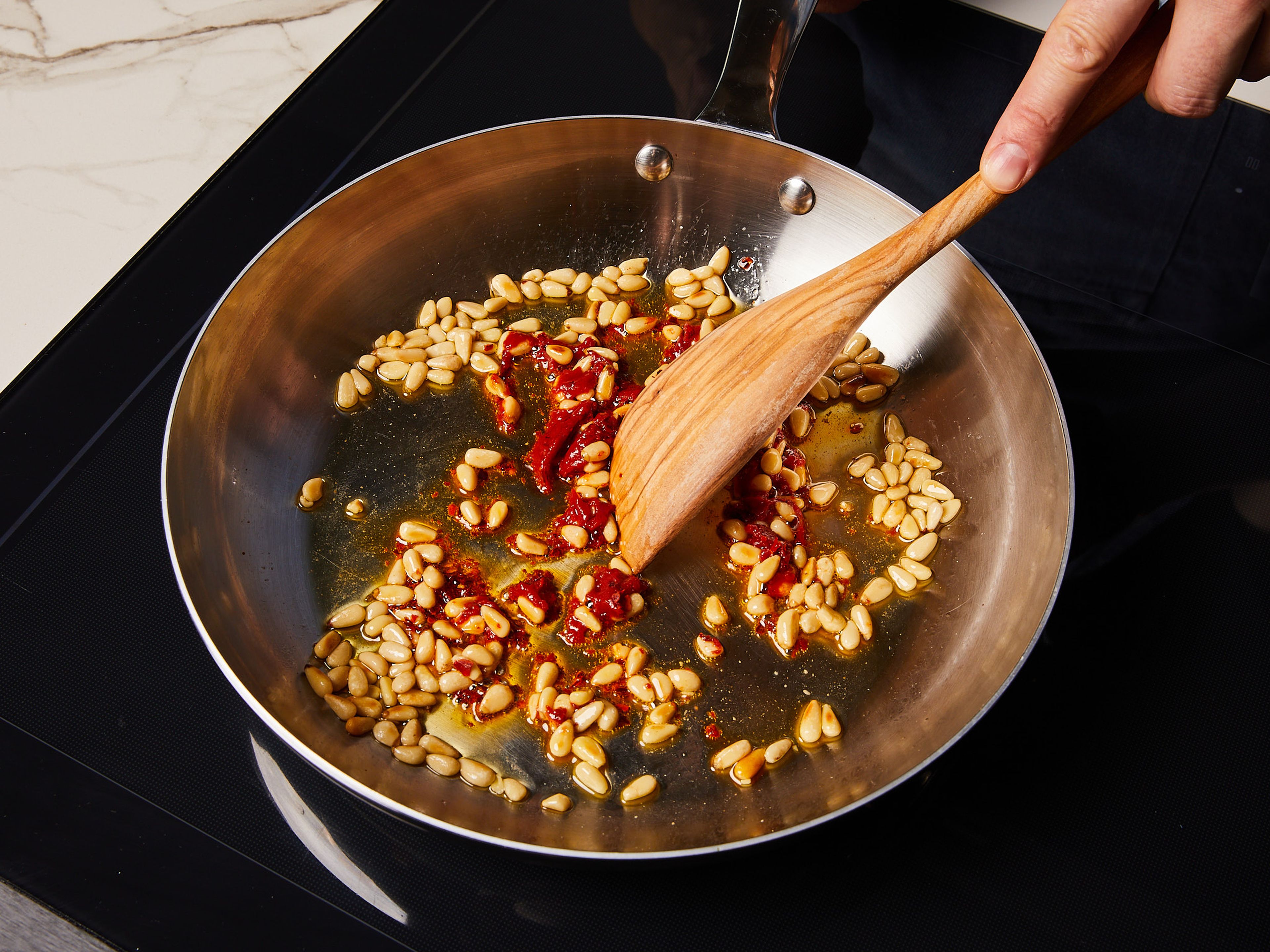 In a frying pan, heat some olive oil over medium heat. Add pine nuts, fry for approx. 2 min. until the nuts take on some color. Reduce heat to medium low, add tomato paste and chili flakes. Fry until the tomato paste is darkened, set aside to cool. In the meantime, grate Parmesan cheese. Set a large pot of water to boil.