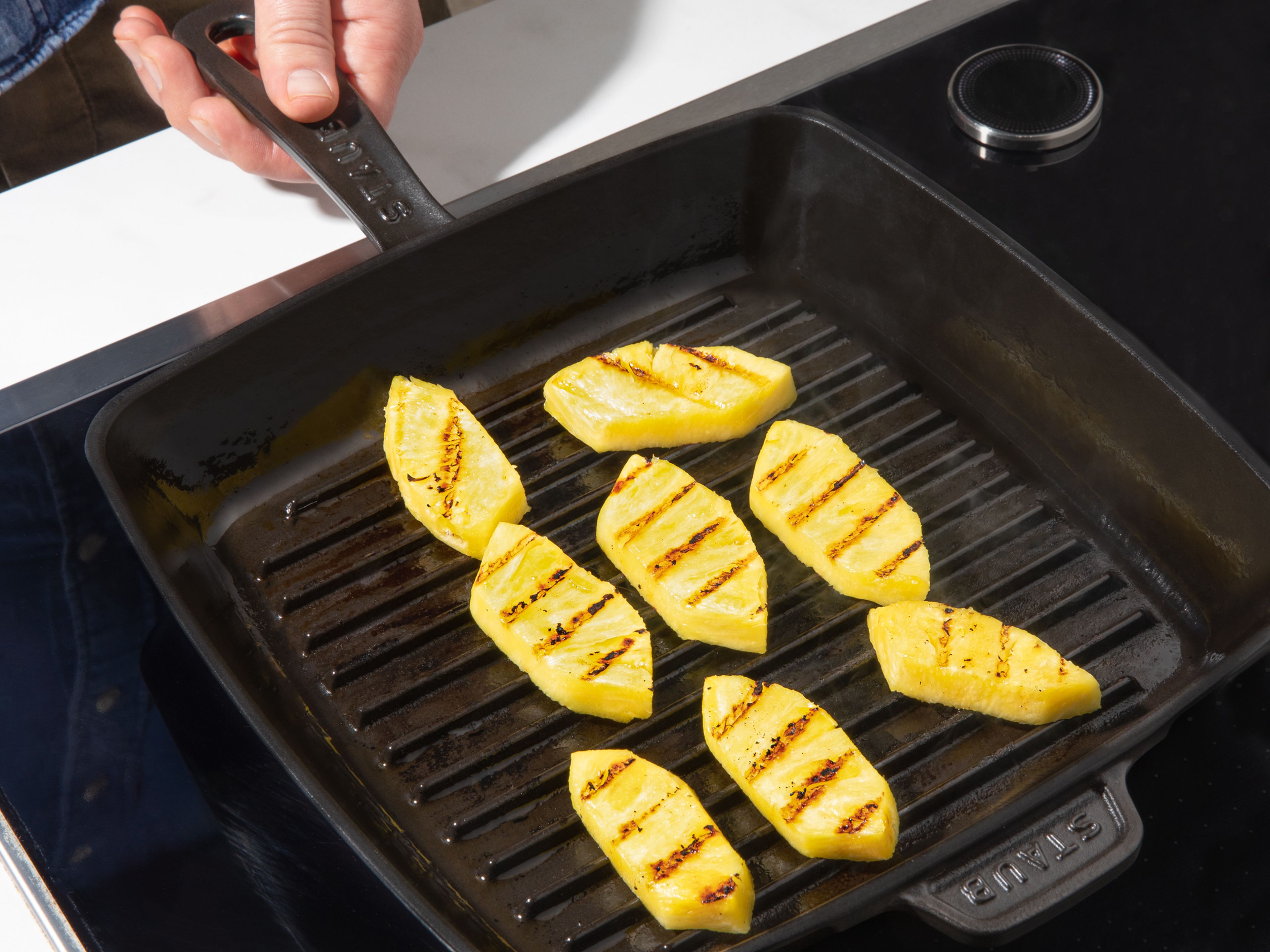 In einer Grillpfanne die Ananasstücke grillen, bis sie etwas Flüssigkeit lassen und sich goldbraun färben. Die Ananasstücke aus der Pfanne entfernen.