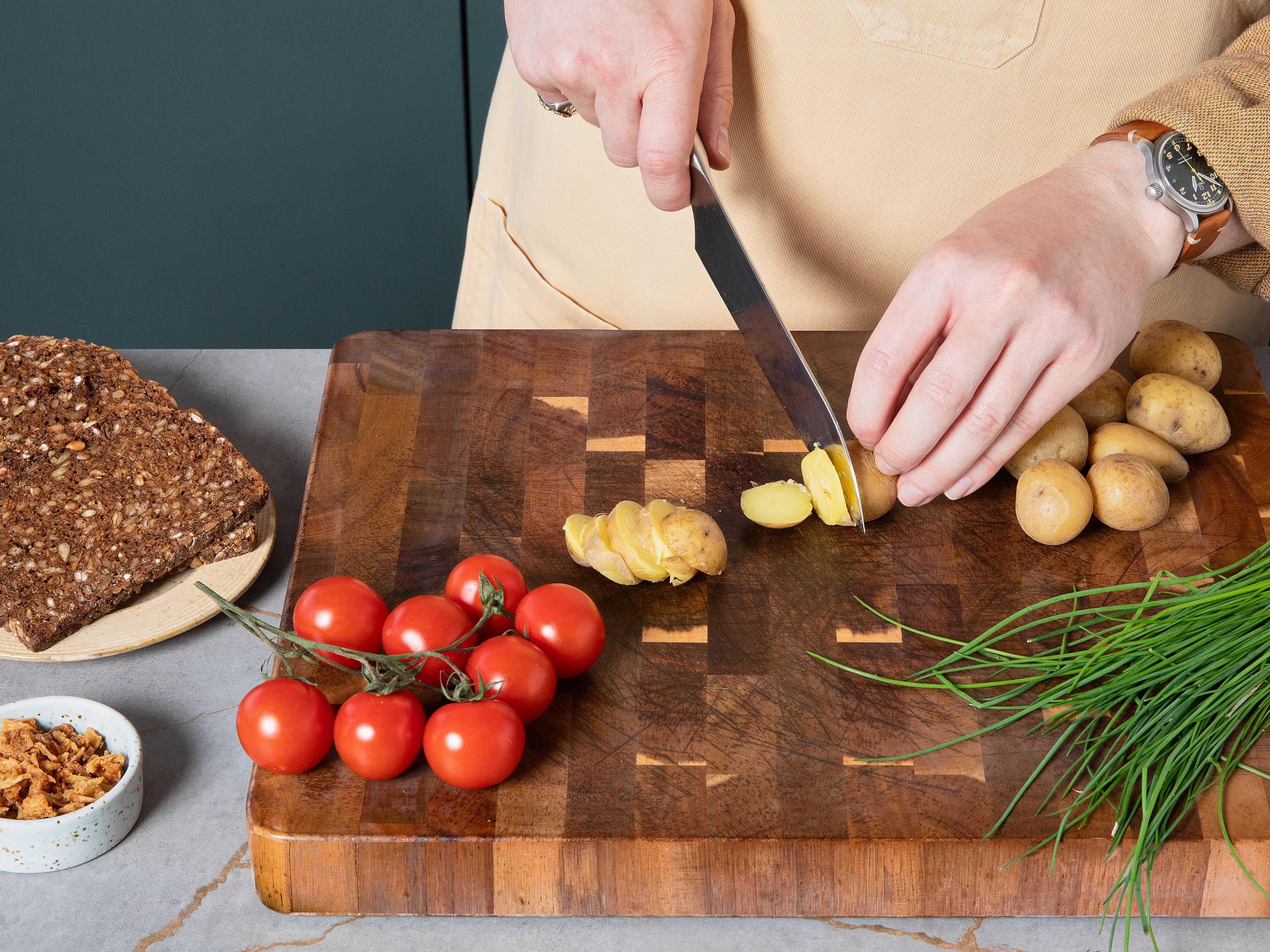 Für das Kartoffel-Tomaten-Smørrebrød: Bestreiche jede Brotscheibe großzügig mit Butter. Schneide dann gekochte Kartoffeln und Tomaten von möglichst ähnlicher Größe in ca. 0,5 cm dicke Scheiben. Lege die Scheiben abwechselnd – also Kartoffel, dann Tomate – auf die beiden Brotscheiben. Würze alles mit Salz und Pfeffer, beträufle es mit Mayonnaise und streue zum Schluss knusprige Röstzwiebeln und Schnittlauch darüber.
