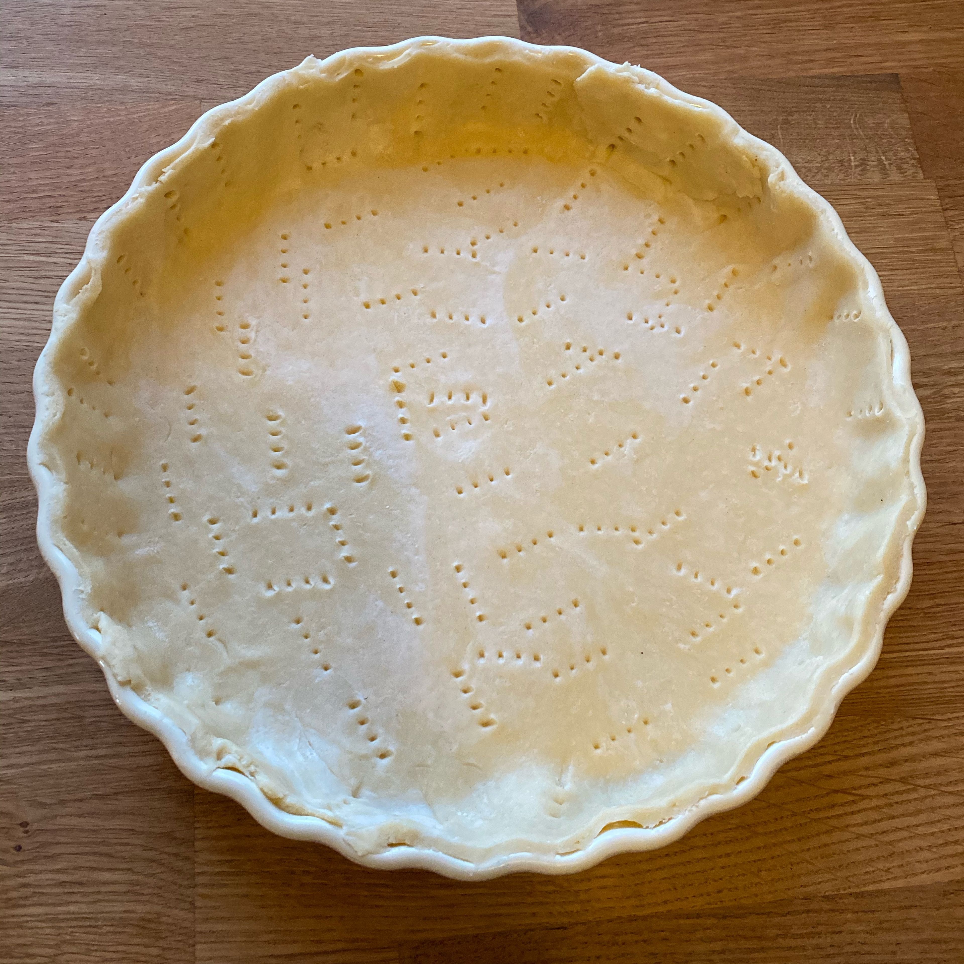 Kuchenform buttern, Teig aus dem Kühlschrank nehmen und mit etwas Mehl ausrollen, in der Kuchenform auslegen, Teig mit Gabel einstechen.