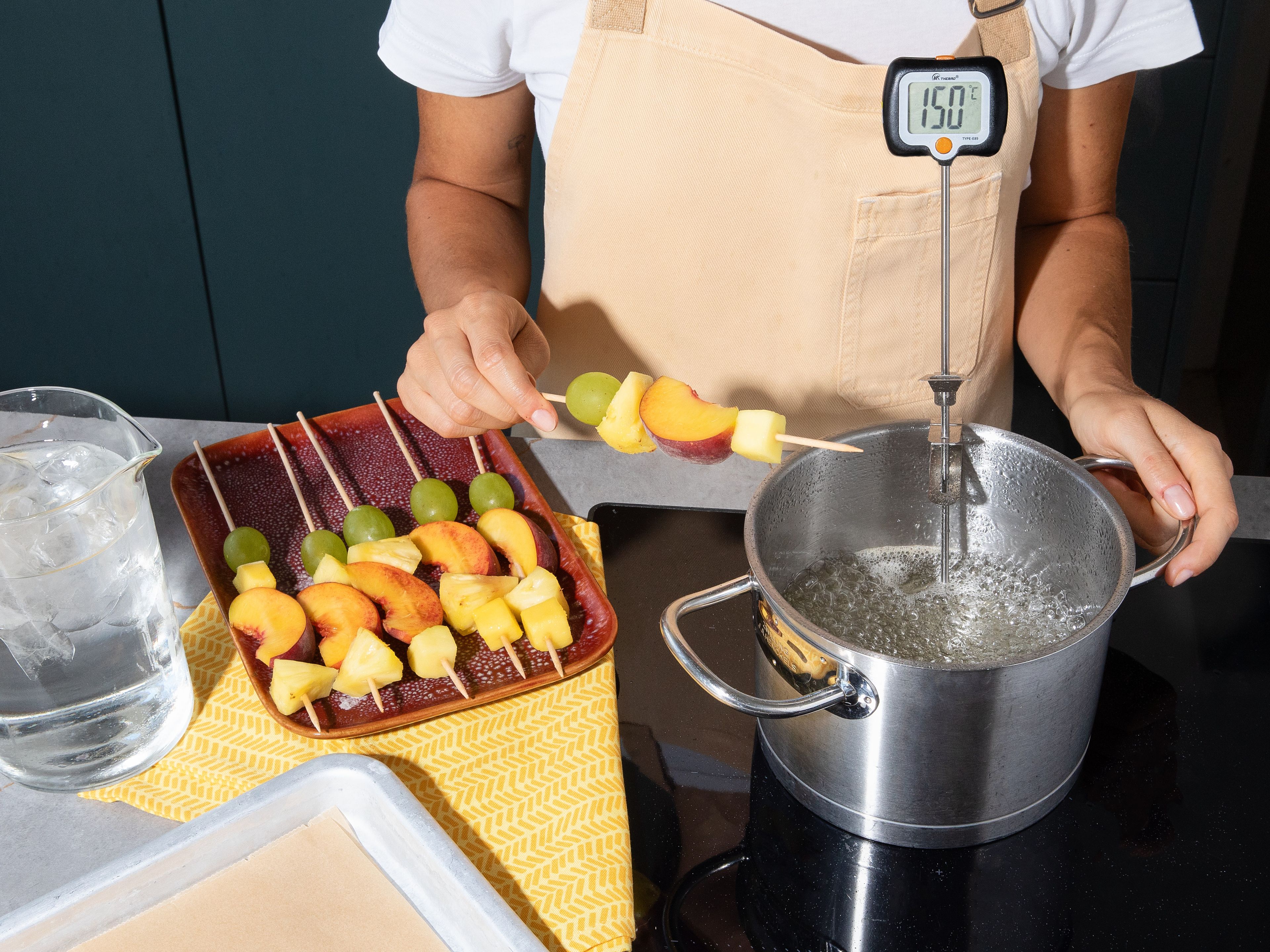 Ein Backblech mit Backpapier auslegen. Zucker in einen Topf geben, mit Wasser bedecken und den Zitronensaft hinzufügen. Darauf achten, dass der gesamte Zucker befeuchtet ist, dabei aber auf keinen Fall umrühren. Ein Zuckerthermometer in den Topf stellen und die Mischung bei mittlerer bis hoher Hitze ca. 30–35 Min. erhitzen, bis der Zucker eine Temperatur von 150°C erreicht hat. Die Temperatur sollte 150°C nicht überschreiten. Ein hohes Gefäß mit kaltem Wasser und Eiswürfeln füllen. Um zu testen, ob der Zucker fertig ist, das Ende eines Holzspießes kurz hineintauchen und anschließend in das Eiswasser tauchen. Wird der Zucker dabei sofort fest, ist er fertig. Den Topf vom Herd nehmen.