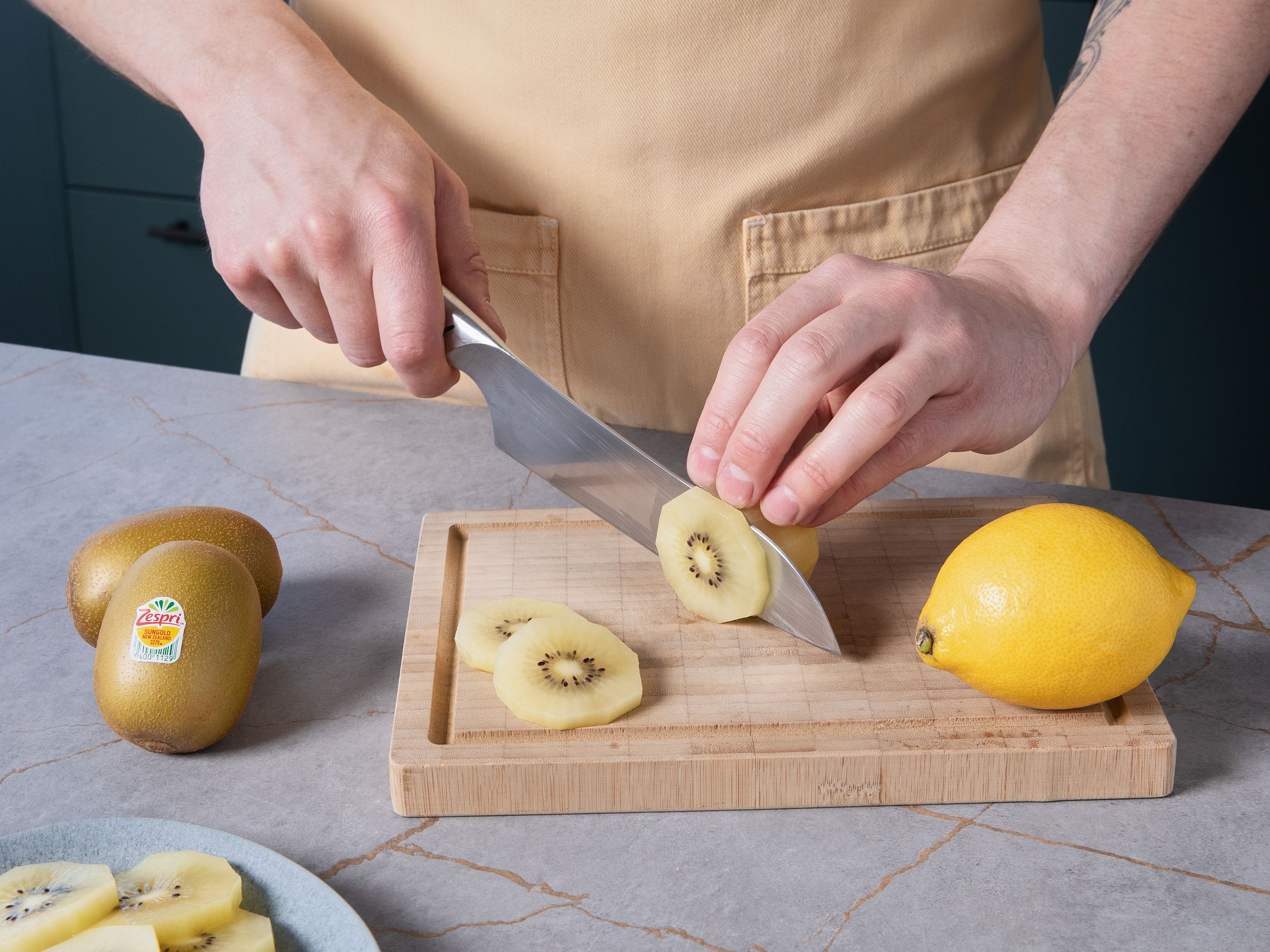 Die Zespri™ SunGold™ Kiwis schälen und in feine Scheiben schneiden. Die Zitrone heiß abwaschen, trocken reiben, etwas Schale fein abreiben und den Saft auspressen.