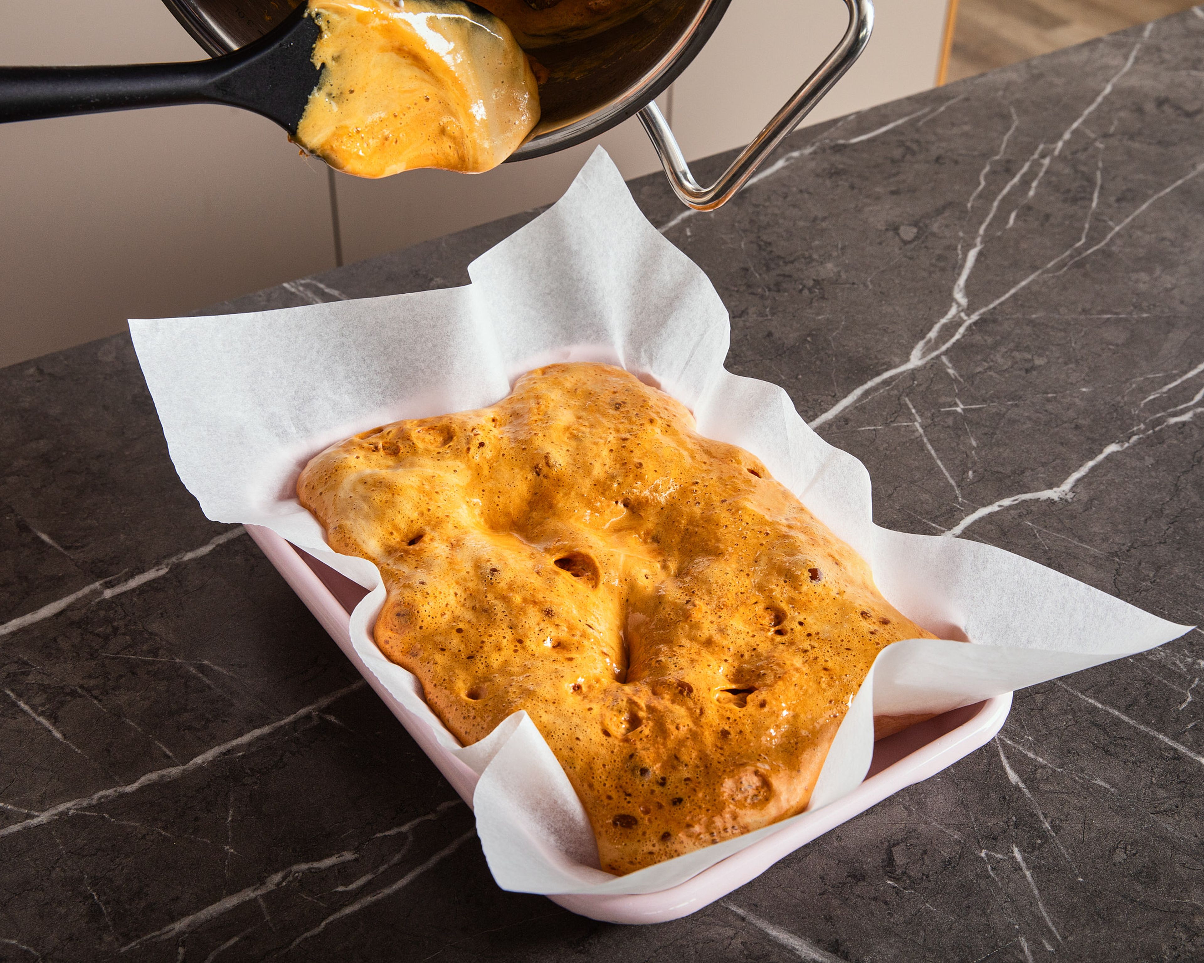 In the meantime, line a fairly high baking dish (min. 20 cm × 20 cm) with baking paper. As soon as the sugar mixture reaches 150°C/302°F, take the pan off the heat, add in baking soda and stir it in evenly. Do not stir too vigorously, otherwise the mixture will be too smooth and the honeycomb will lose the bubbles. The mixture should start to bubble strongly and turn gold in color. after approx. 30 secs., pour the mixture onto the baking dish. Leave to harden for approx. 1 hr and then break by hand or with a knife. Optionally, dip in melted chocolate and sprinkle with sea salt flakes.