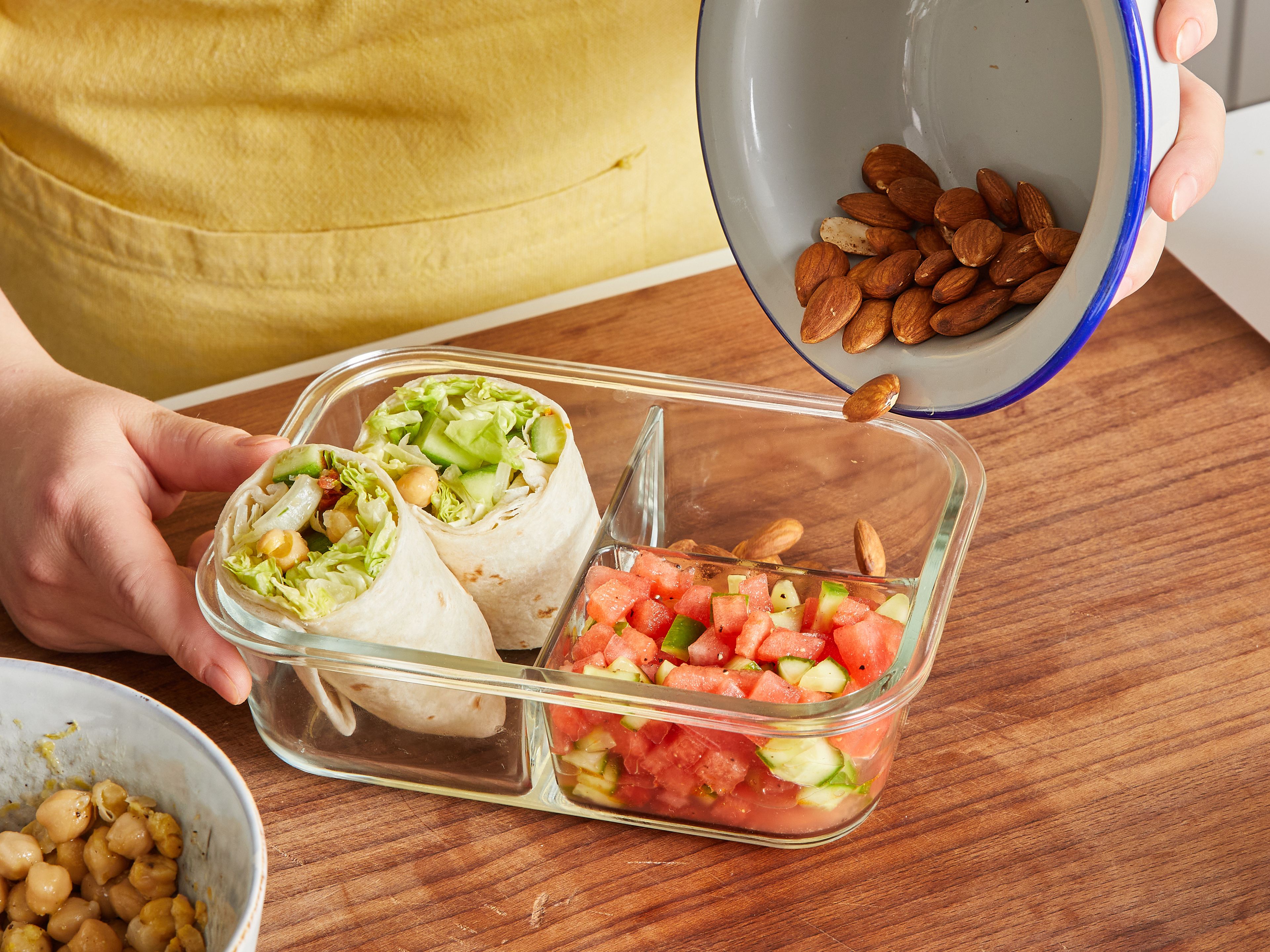 For the first lunch box: Mix diced cucumber and melon with remaining olive oil and some juice of the remaining, halved zested lemon; season with salt and pepper. Pour into a small compartment of a divided lunch box. Spread two tortilla wraps with 1 tbsp of the yogurt cream. Then top evenly with ⅓ of the lettuce leaves, ⅓ of the coarse diced cucumber, half of the sun-dried tomatoes, and half of the whole chickpeas. Roll up tightly and cut in half, then pack into the lunch box. Put the remaining whole almonds into a small compartment of the lunch box.