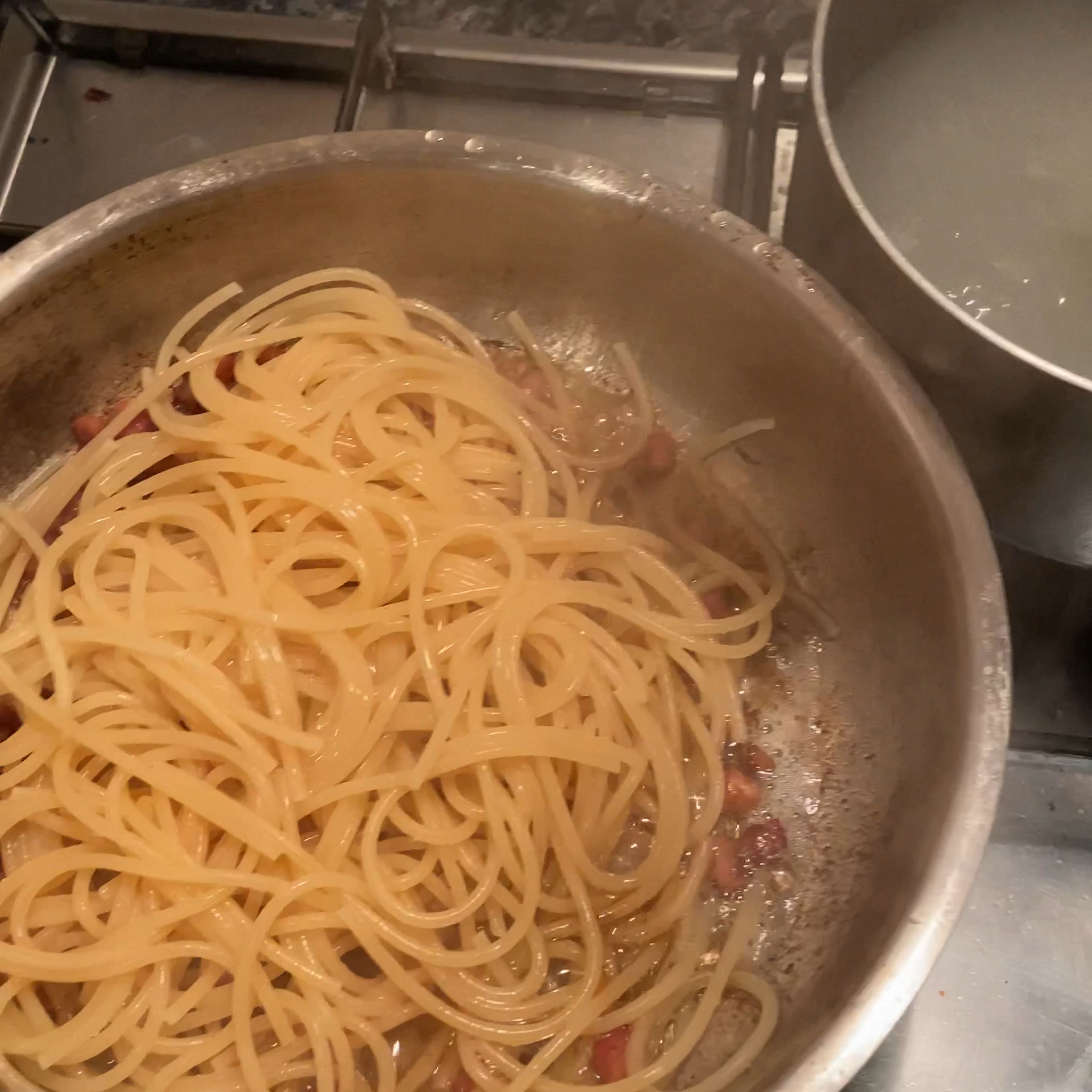 Turn off all heat sources once pasta is aldenté. Using tongs, place the spaghetti into the pancetta with a little of the starch water. Keep stirring and mixing until any sizzling has stopped. 