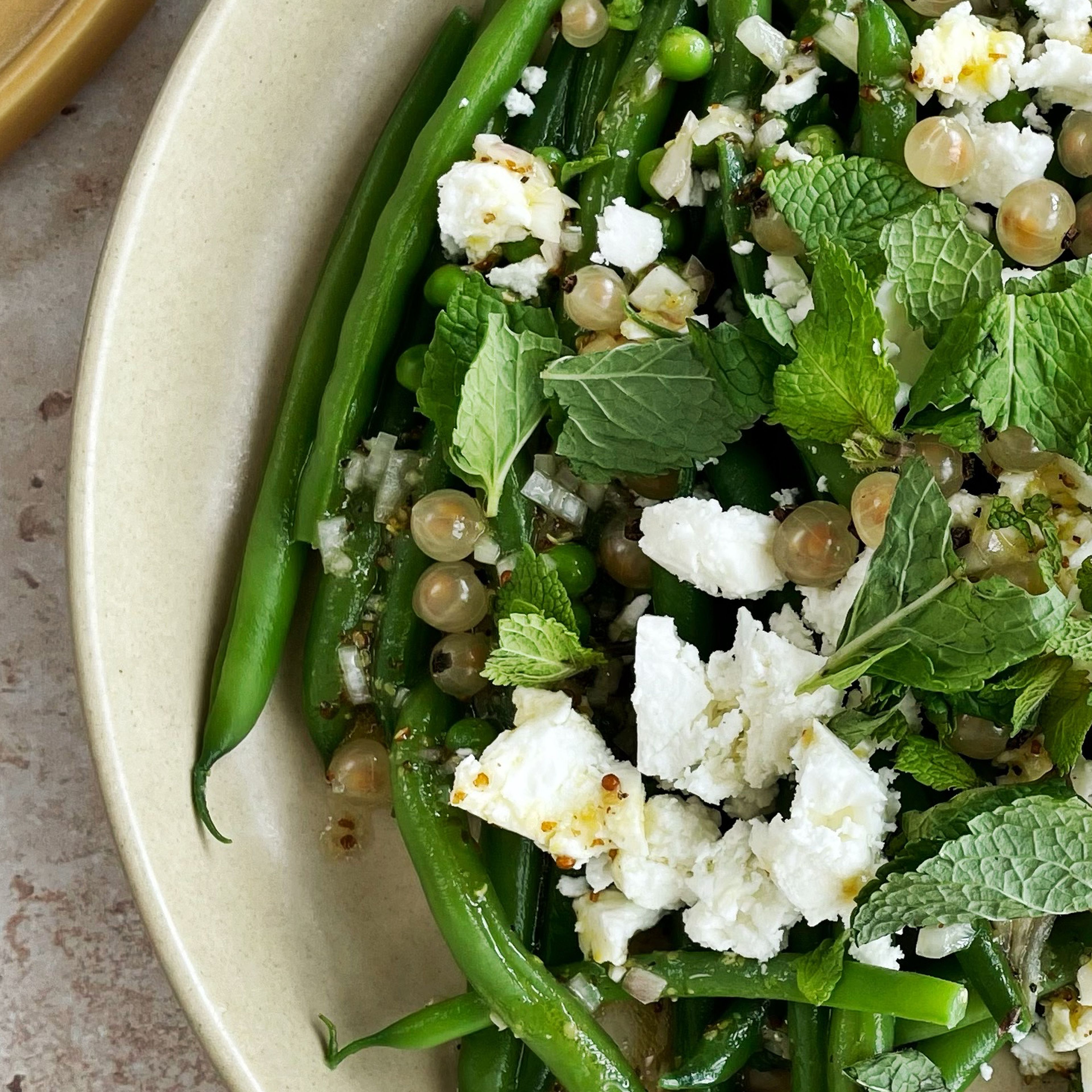 Arrange the beans and peas on a large plate. Top with feta cheese and currants and garnish with mint.