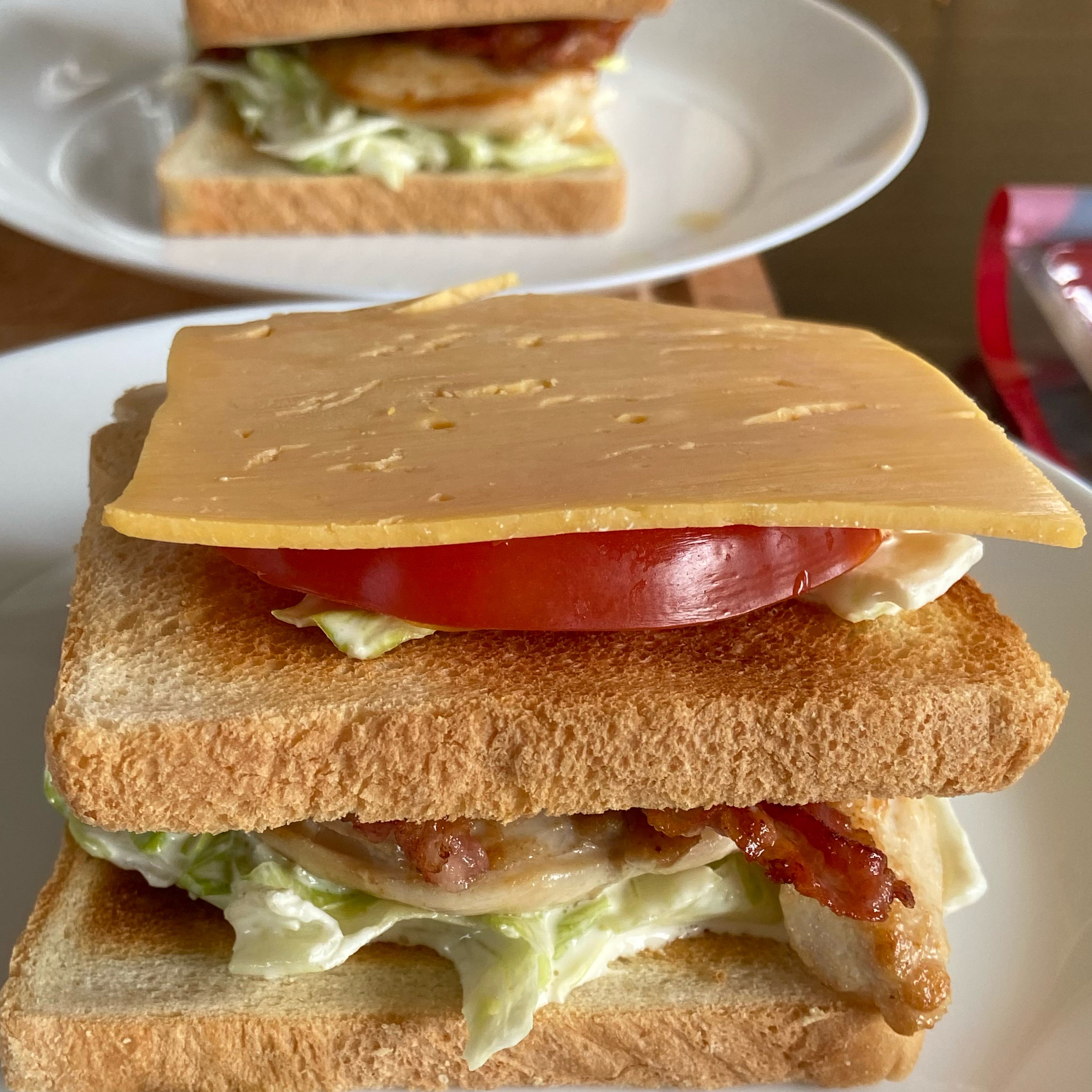 Add another generous portion of lettuce with the sauce on top of the second bread slice, add a tomato slice (or two) and top with a slice of cheddar cheese.