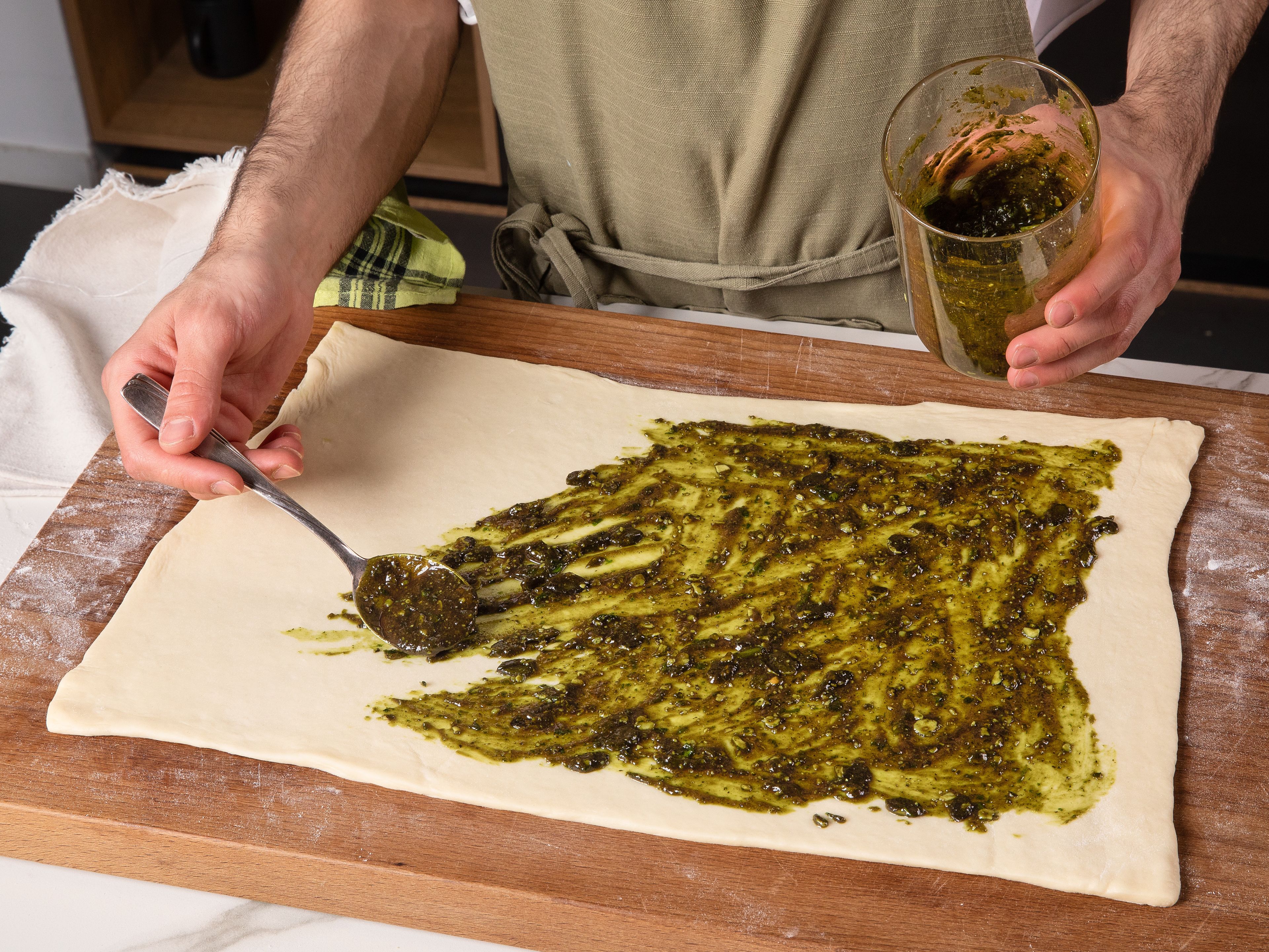 Roll yeast dough out and place on a lightly floured surface, roll out to form a rectangle if needed, approx. 30–40 cm wide. Spread wild garlic pesto evenly over it, leaving approx. 1 cm/0.4 in. of space around the borders.