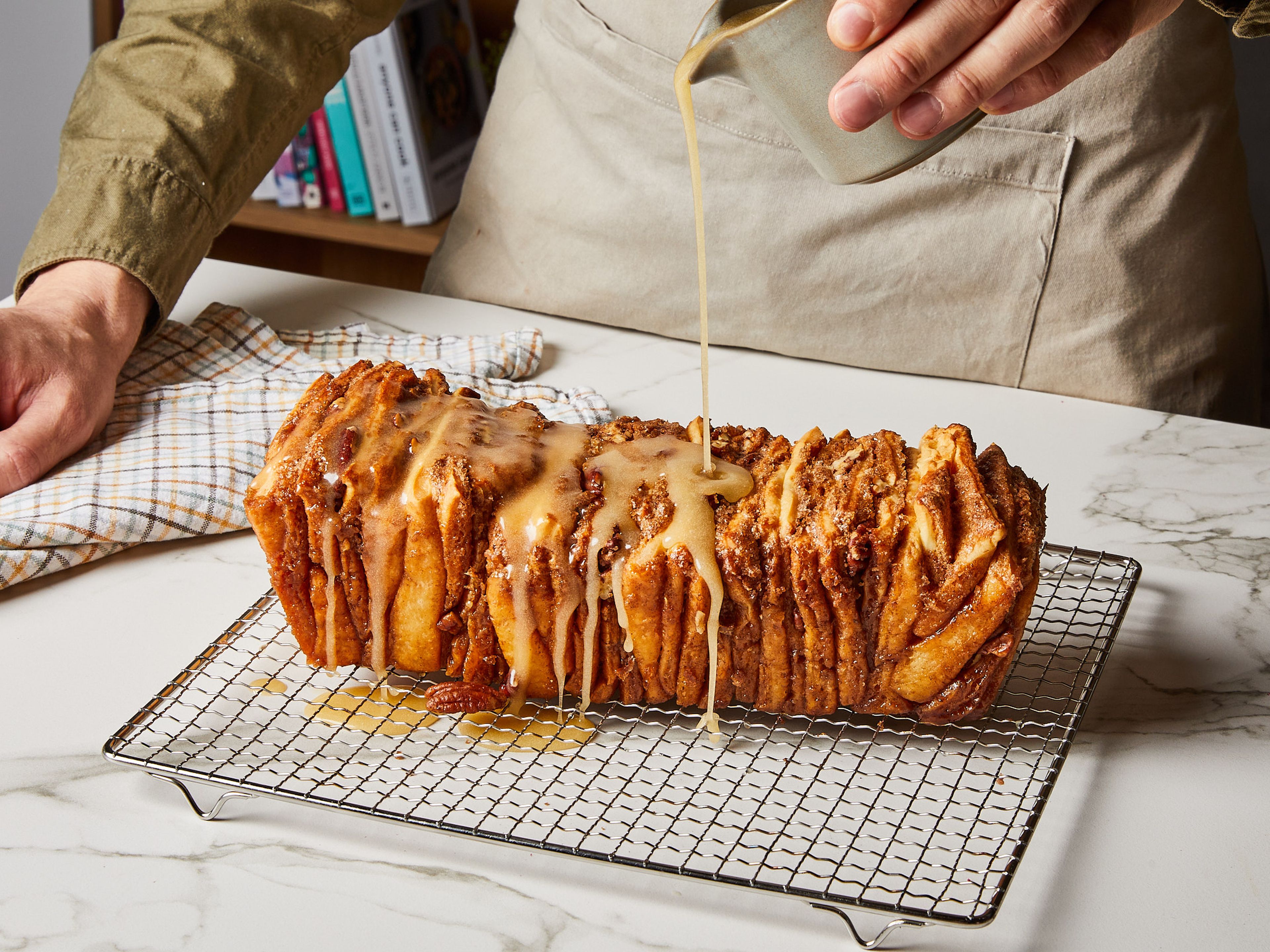 Das Zupfbrot im vorgeheizten Ofen bei 175 °C Ober- / Unterhitze für etwa 40 Min. backen, bis die Oberseite leicht gebräunt ist und das Zentrum durchgebacken aussieht. Während das Zupfbrot abkühlt, die Glasur zubereiten. Dazu Puderzucker, Wasser, geschmolzene Butter und Ahornsirup verrühren. Das Zupfbrot auf eine Servierplatte geben und mit der Glasur bestreichen. Am besten warm genießen!
