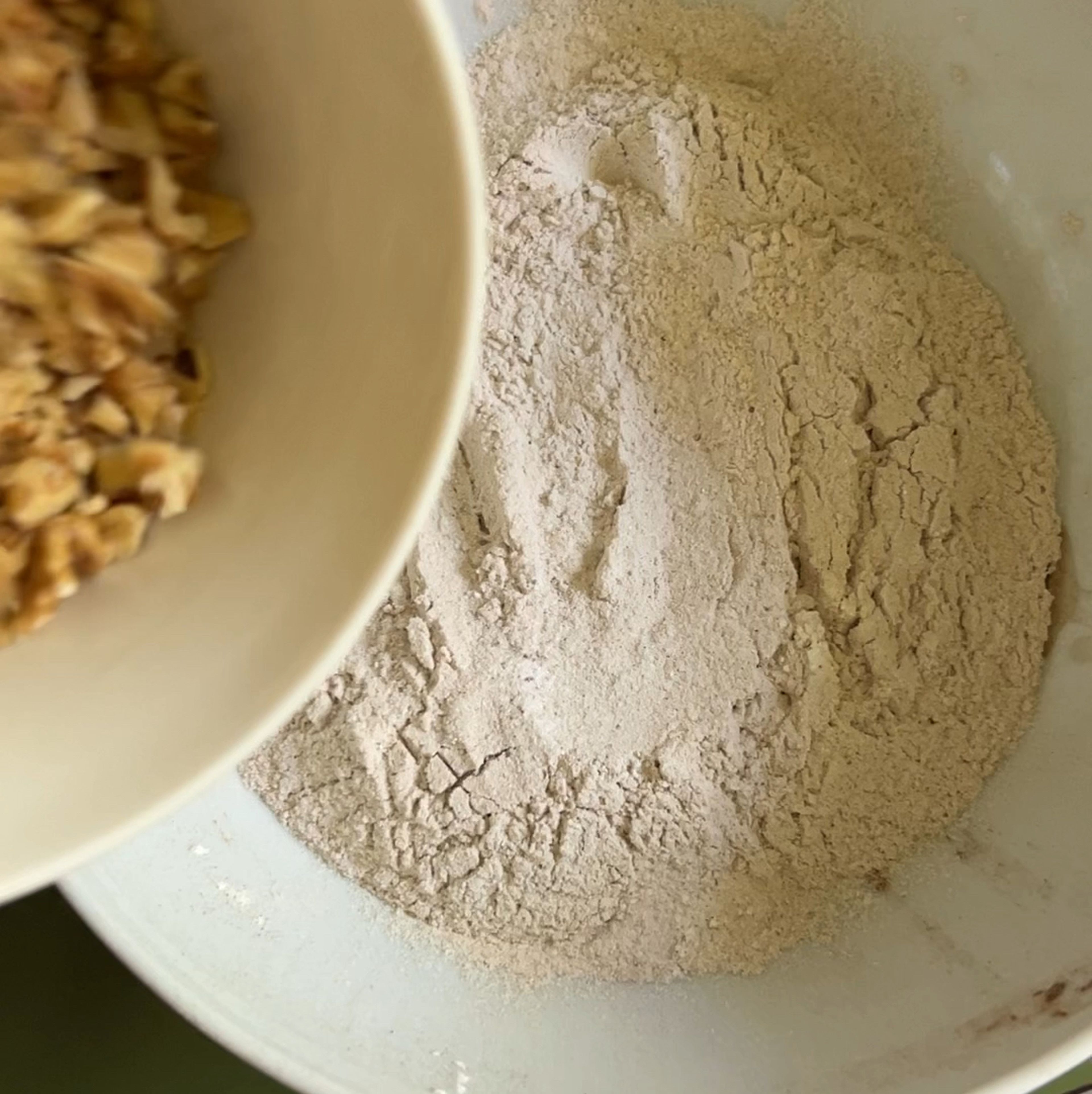 Add chopped walnuts to a bowl with dry ingredients and mix them with your hand.