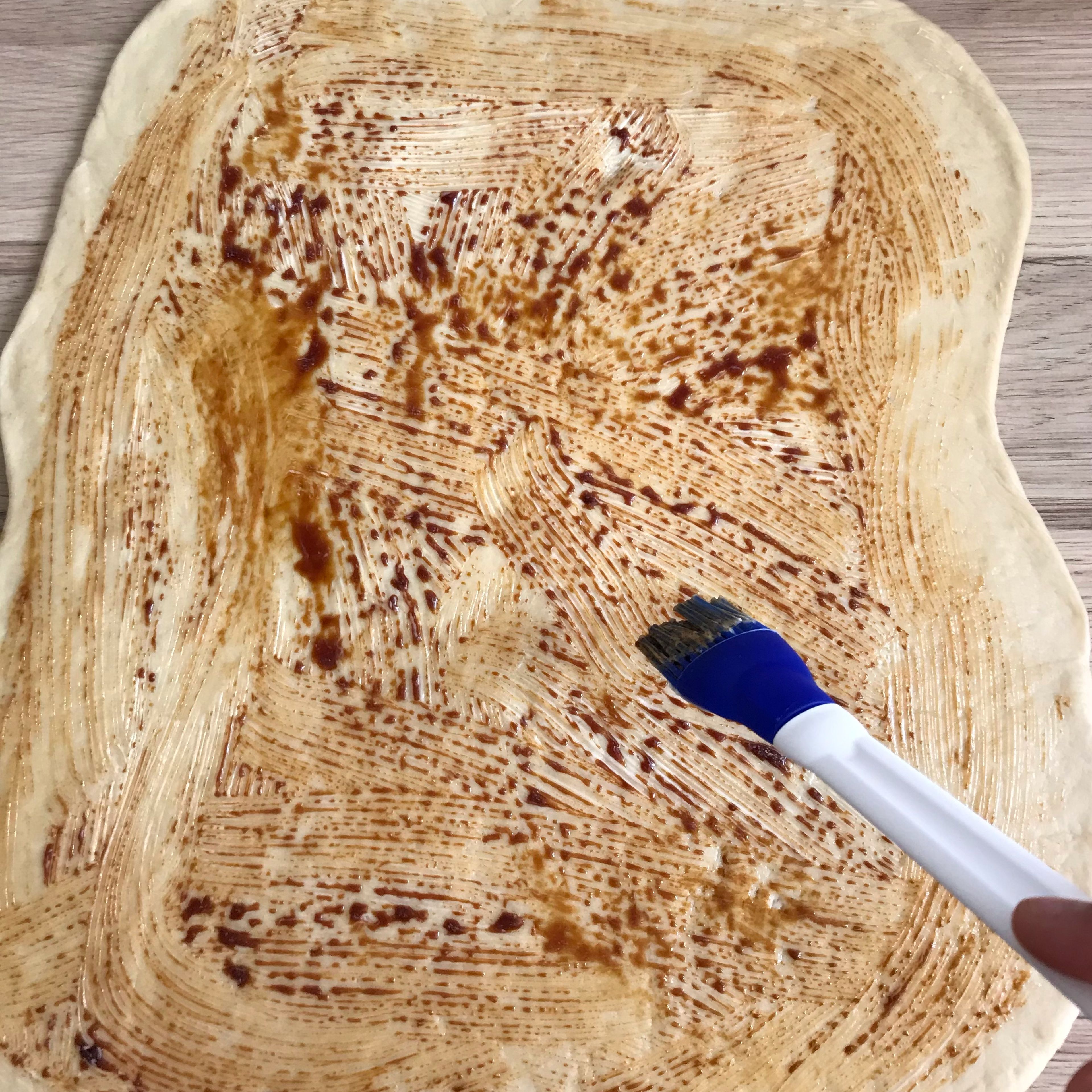 Den Teig auf der Arbeitsplatte 30 x 50 cm ausrollen. Mit weicher Butter und Traubensirup bestreichen.