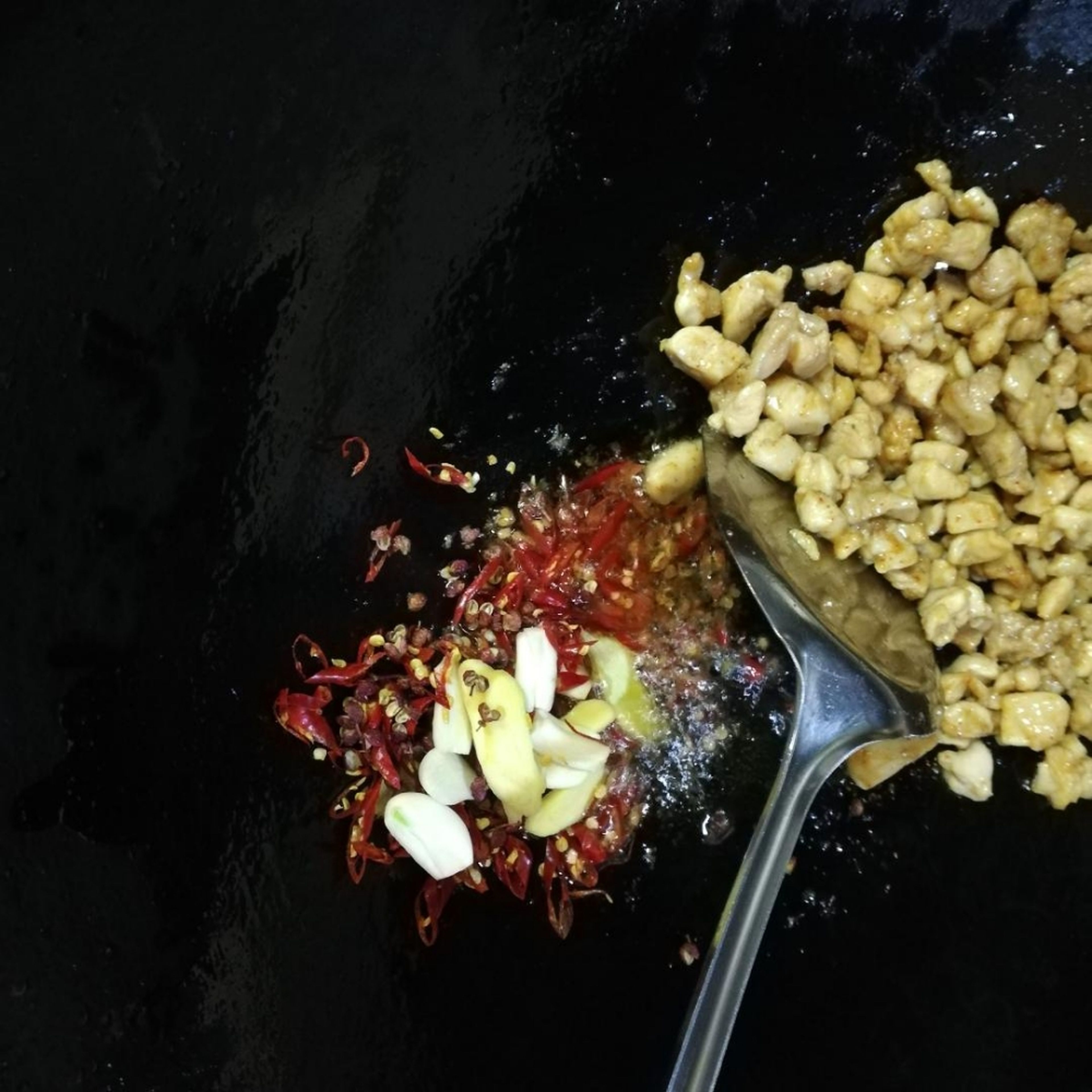 Den Knoblauch, Ingwer, getrocknete Chilis und die Szechuanpfefferkörner in den Wok geben und weiterbraten.