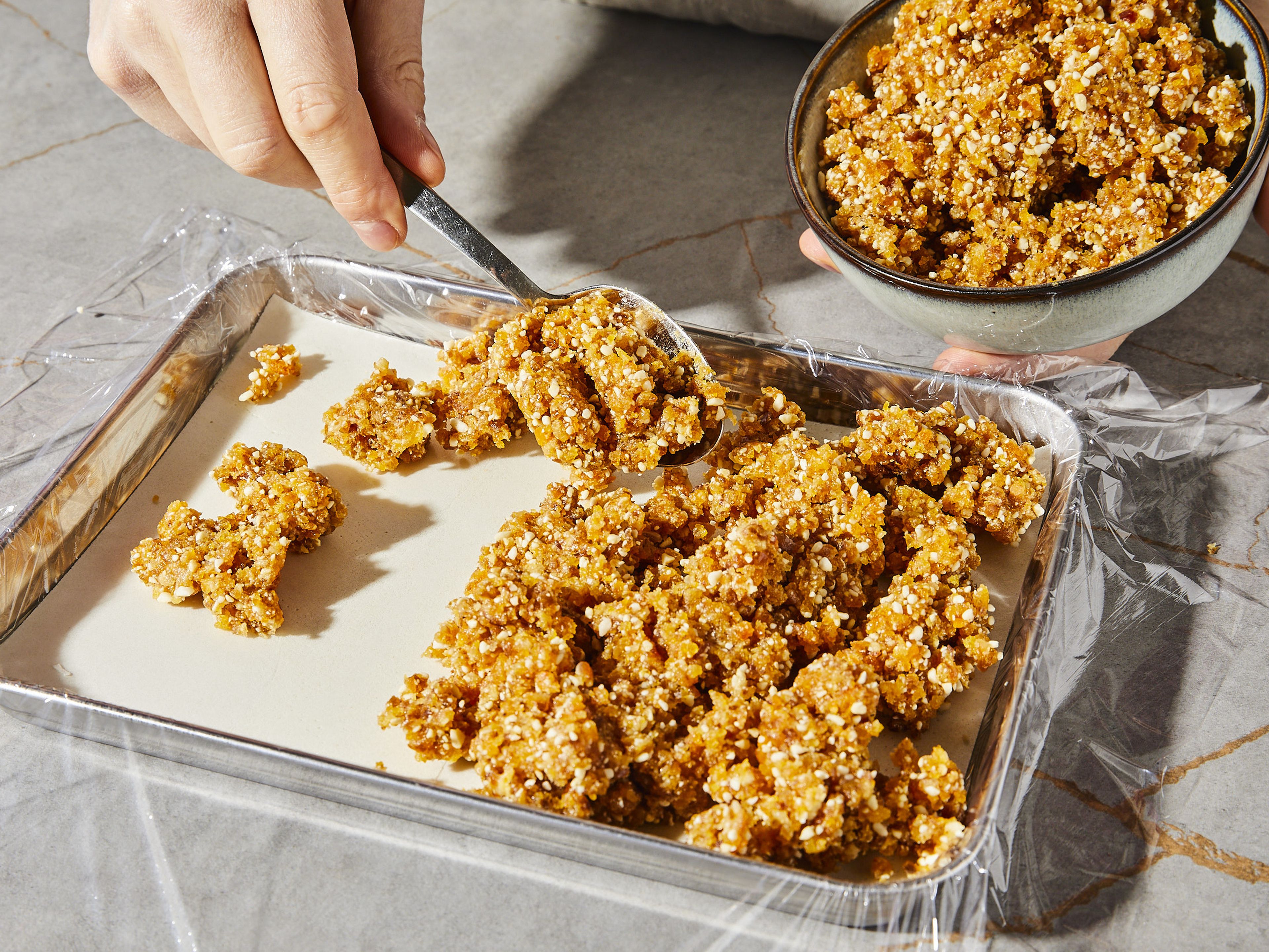 Eine Auflaufform mit Klarsichtfolie auslegen, sodass die Ränder überlappen. Die Masse hinein füllen und flach drücken. Die Folien-Überhänge darüber klappen und alles fest andrücken, sodass eine kompakte Schicht entsteht. Am besten geht das mit dem Boden eines Glases oder einer Flasche.