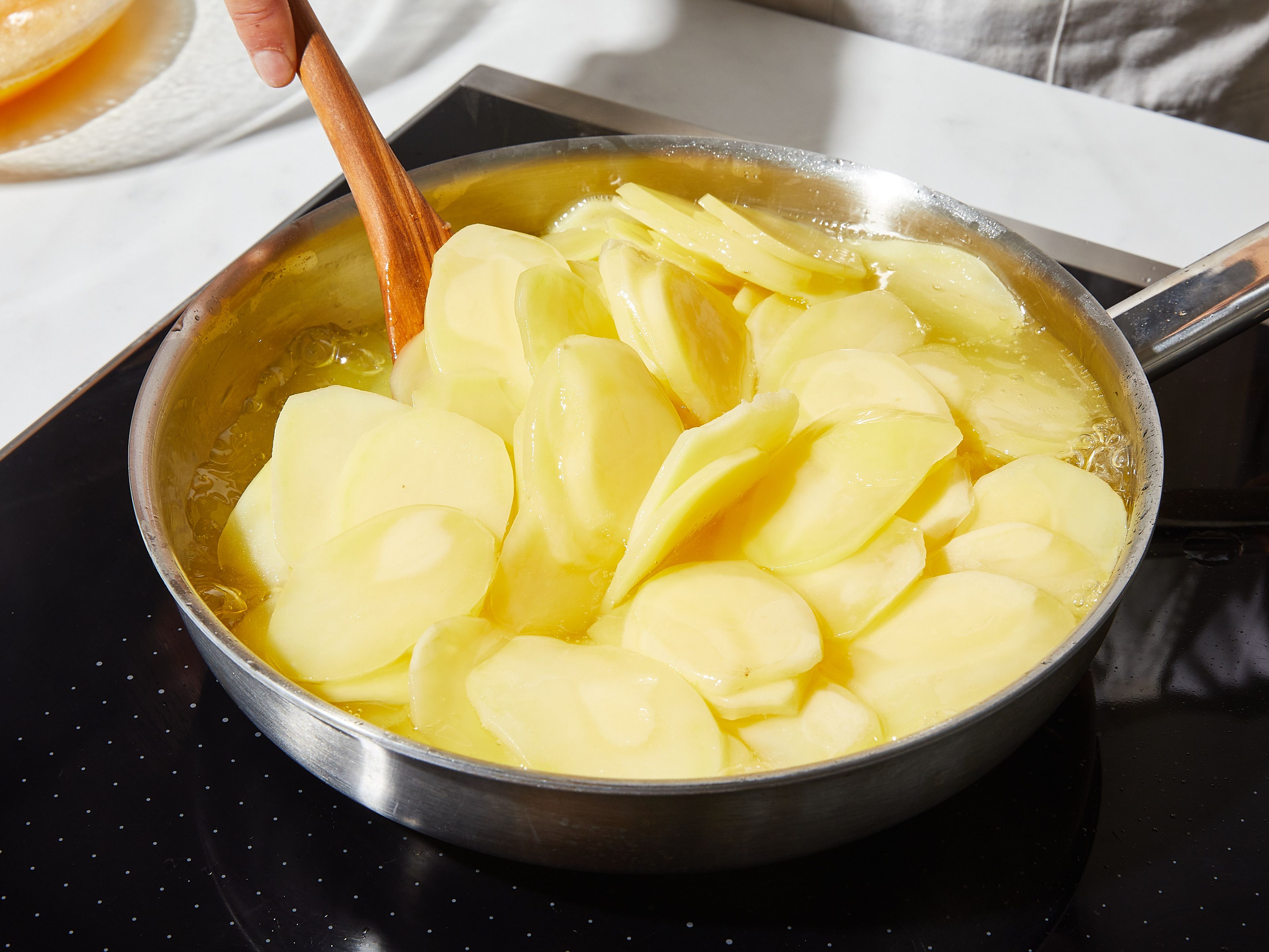 Peel the potatoes and cut into thin slices using a mandoline. Heat the oil in a pan and cook the potato slices for 15 – 20 min. on low heat. If necessary, add a little more oil so they almost float. The potatoes should not take on any color.