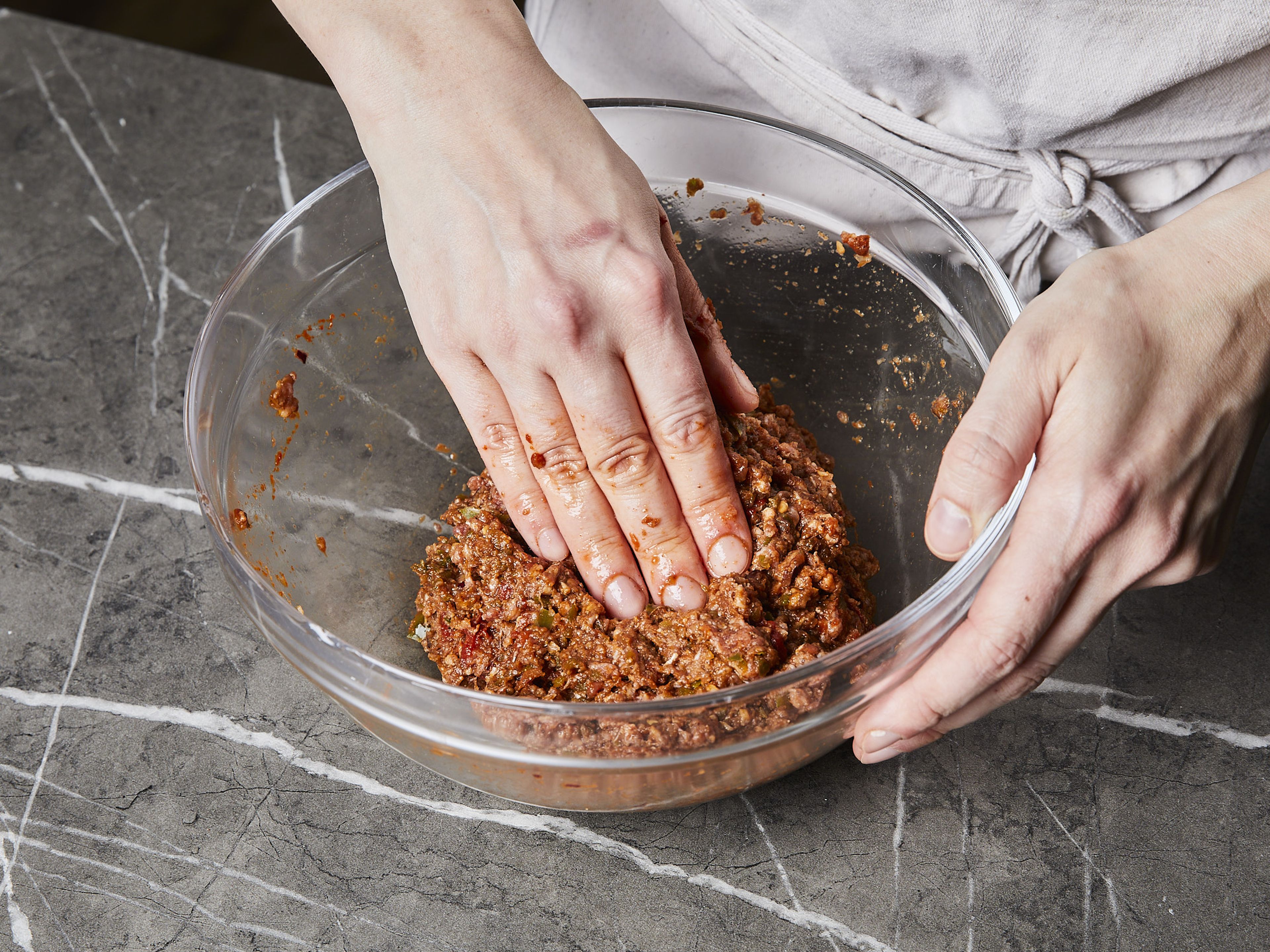 Für die Lahmacun Füllung Zwiebeln schälen und ⅓ der Zwiebeln vierteln. Den Knoblauch schälen. Paprika entkernen und grob würfeln. Die Tomaten vierteln. Dann die Zwiebelviertel, Paprika und Knoblauch fein hacken und mit Biber Salçası, Tomatenmark, gemahlenem Kreuzkümmel, Sumach sowie etwas Salz und Pfeffer vermischen. Alternativ kann dafür auch ein Zerkleinerer verwendet werden. Die Mischung mit dem Rinderhackfleisch, Salz und Pfeffer in eine Schüssel geben und gründlich vermischen.