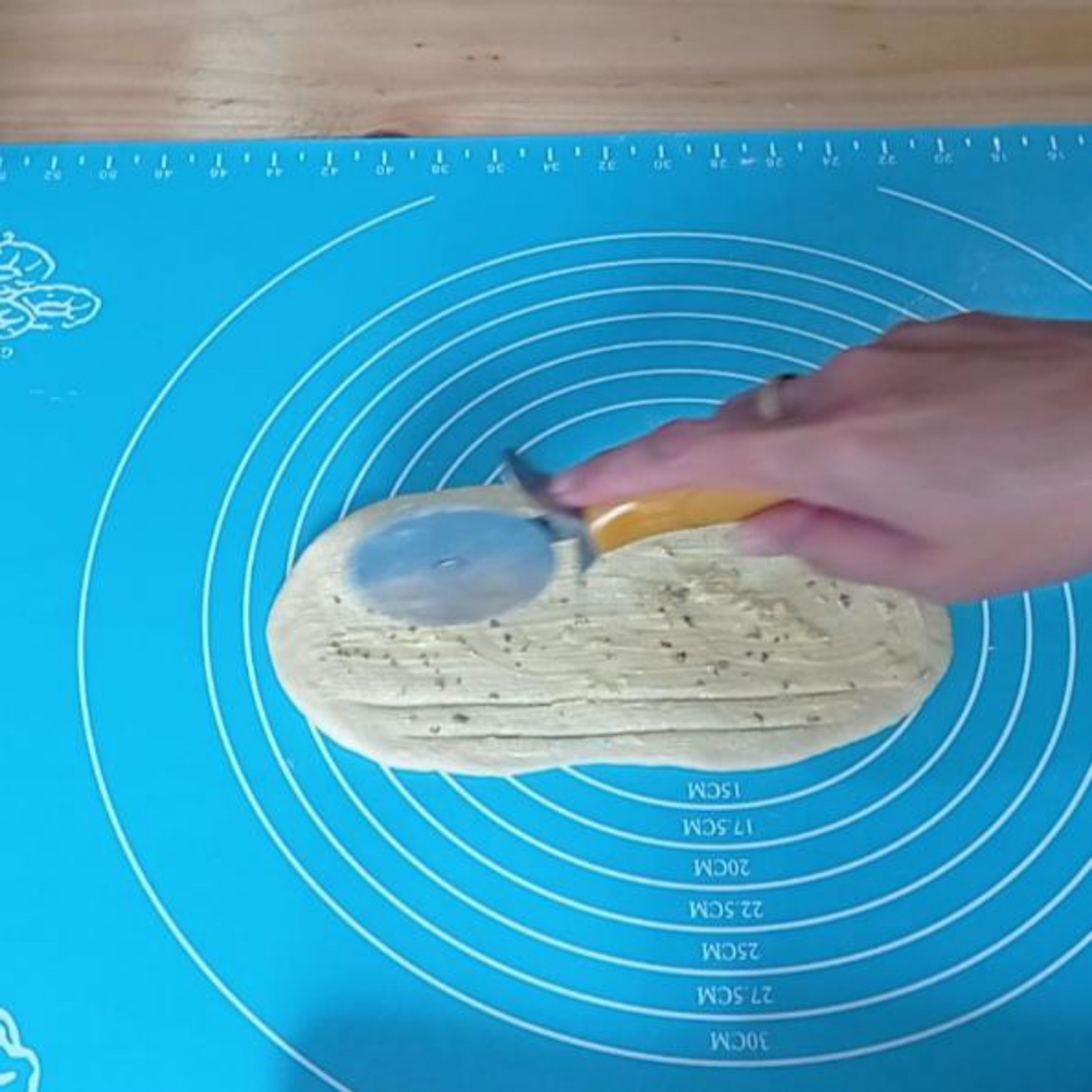 After 10 minutes, open the kitchen towel. Roll out and flatten the dough. Brush with garlic butter paste and use a pizza cutter or knife, you make inner slashes as shown on the picture. Roll from the right side and twist one of the side and pinch the edges of the strips together.