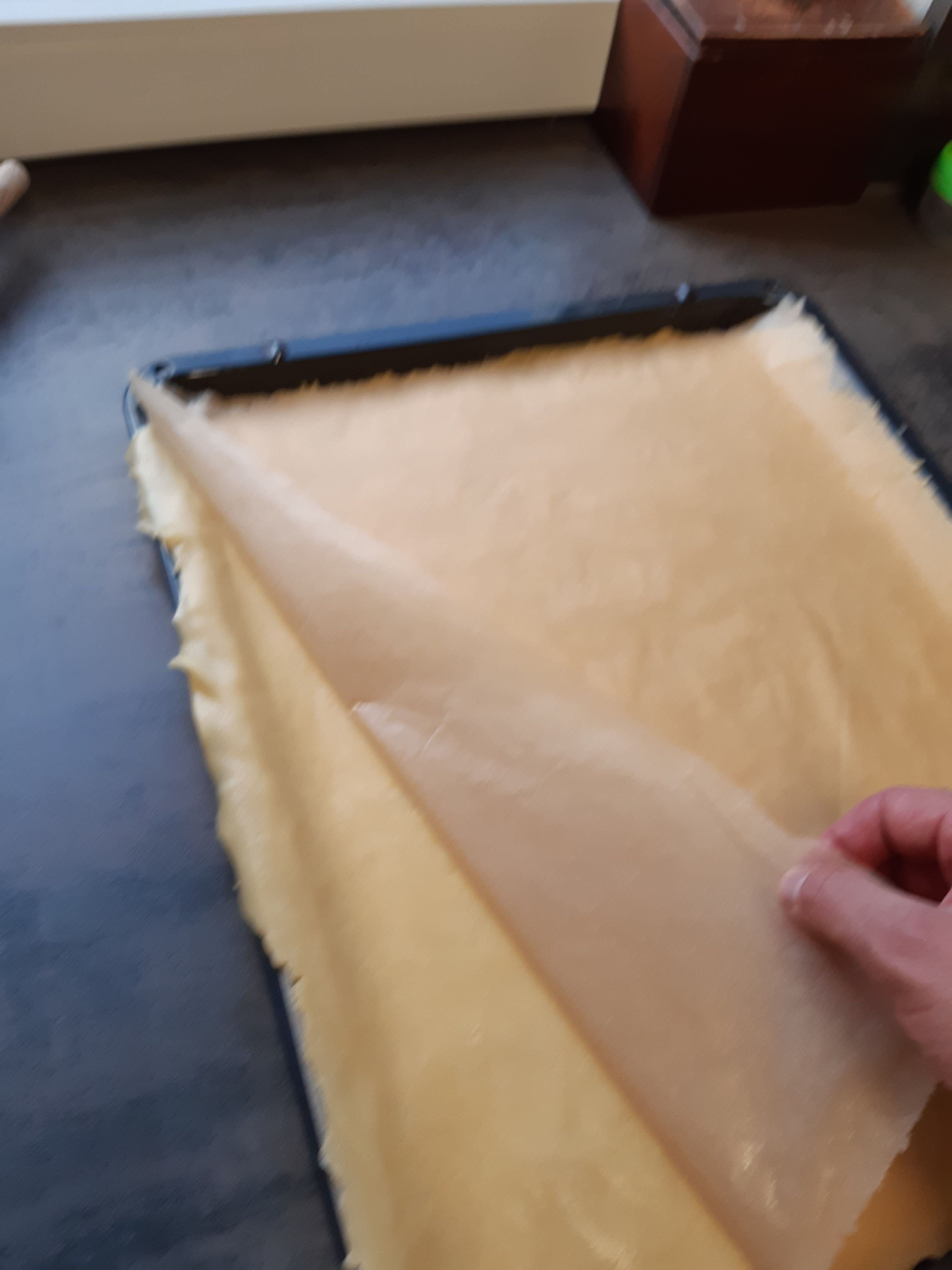Frisches Blatt Backpapier nehmen und die zweite Kugel dünn ausrollen, auch ca. 1-2mm.
Auf die erste Teigschicht mit dem Backpapier nach oben legen und den Teig vorsichtig vom Papier lösen.