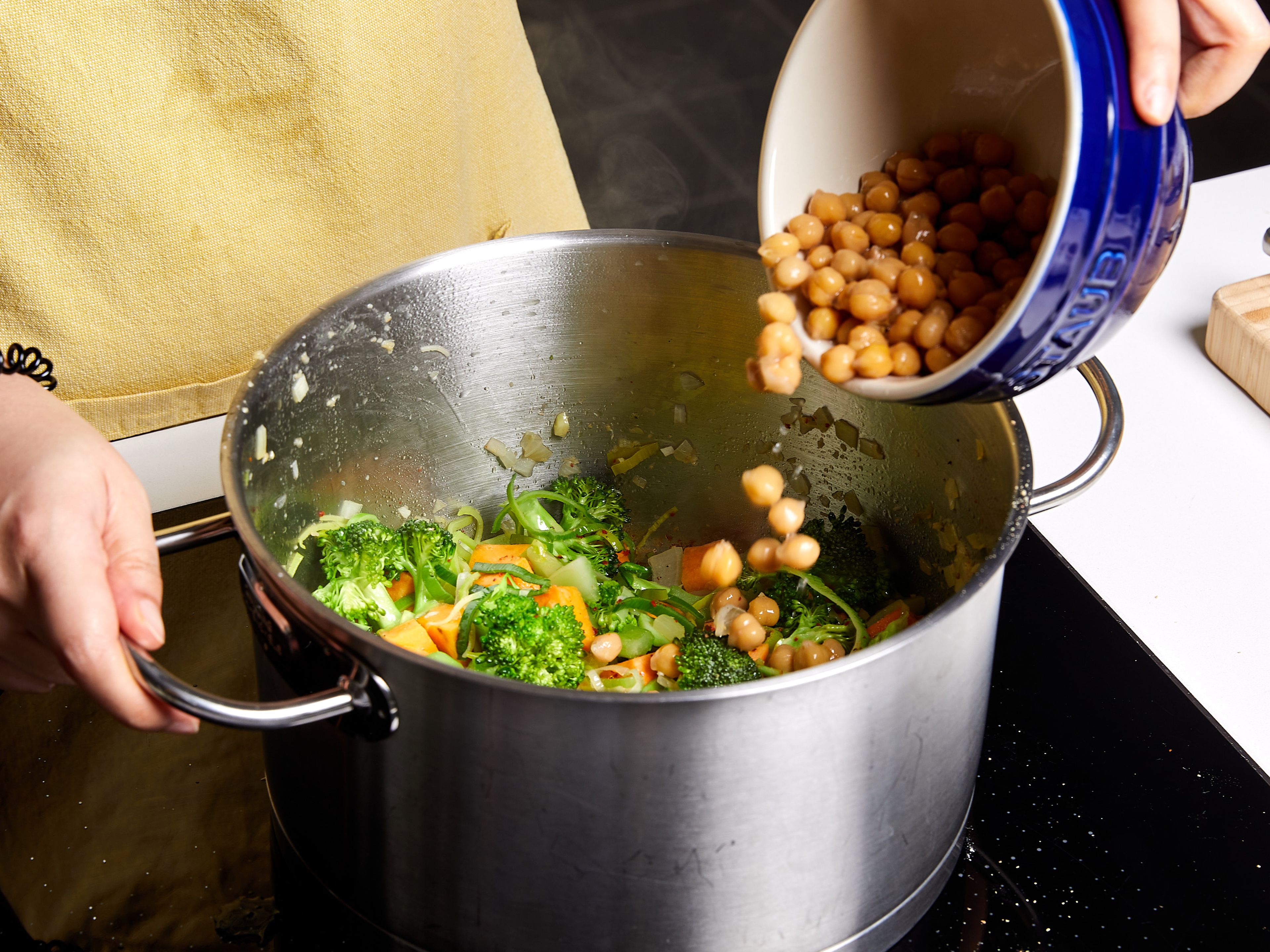 Olivenöl in einem großen Topf auf mittlerer Stufe erhitzen. Zwiebeln und Lauch hinzufügen und glasig dünsten. Knoblauch und Ingwer hinzufügen und kurz mitbraten. Dann Süßkartoffeln, Brokkoli und Sellerie hinzufügen. Mit Salz, Pfeffer und Chiliflocken würzen. Ca. 3 Min. anbraten. Kichererbsen und Gemüsebrühe in den Topf geben und umrühren. Zum Kochen bringen. Dann den Topf abdecken und bei mittlerer Hitze ca. 10–12 Min. köcheln lassen, bis die Süßkartoffeln gar sind.