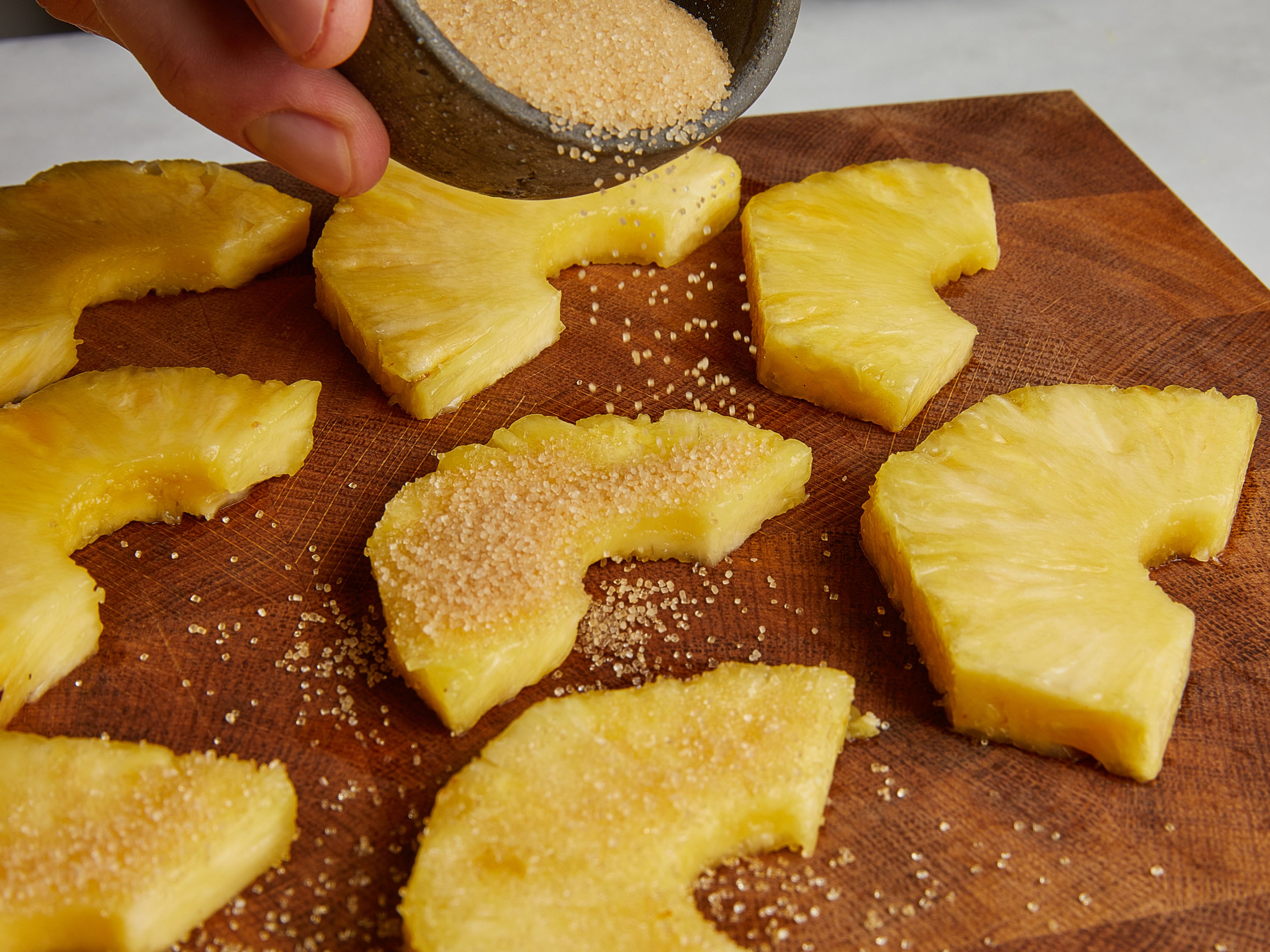 Ananasscheiben von beiden Seiten großzügig mit Zucker bestreuen.