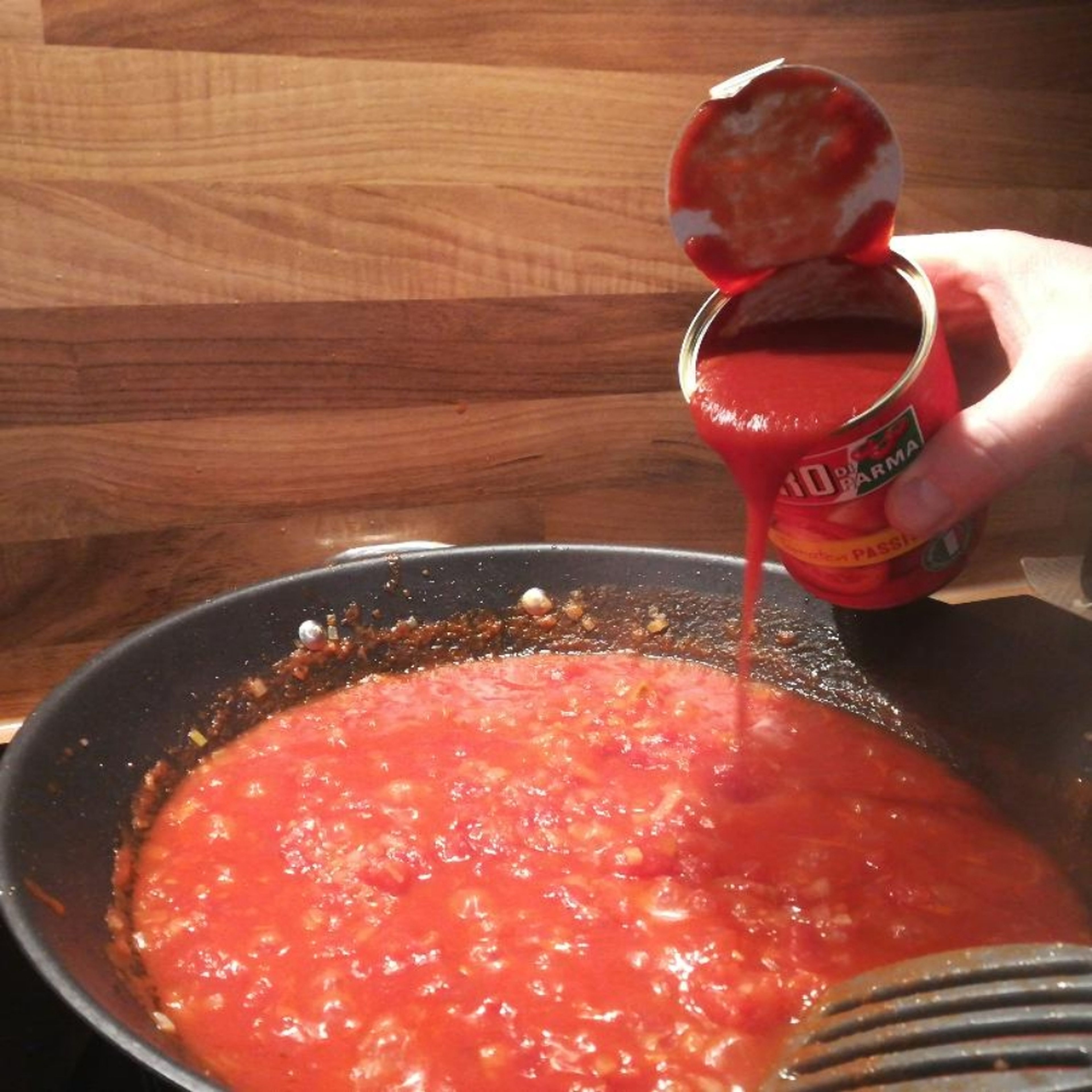 Gehackte Tomaten zu den Zwiebel geben, verrühren und 5 Minuten köcheln lassen. Danach die passierten Tomaten hinzugeben. Mit Basilikum, Oregano abschmecken.
