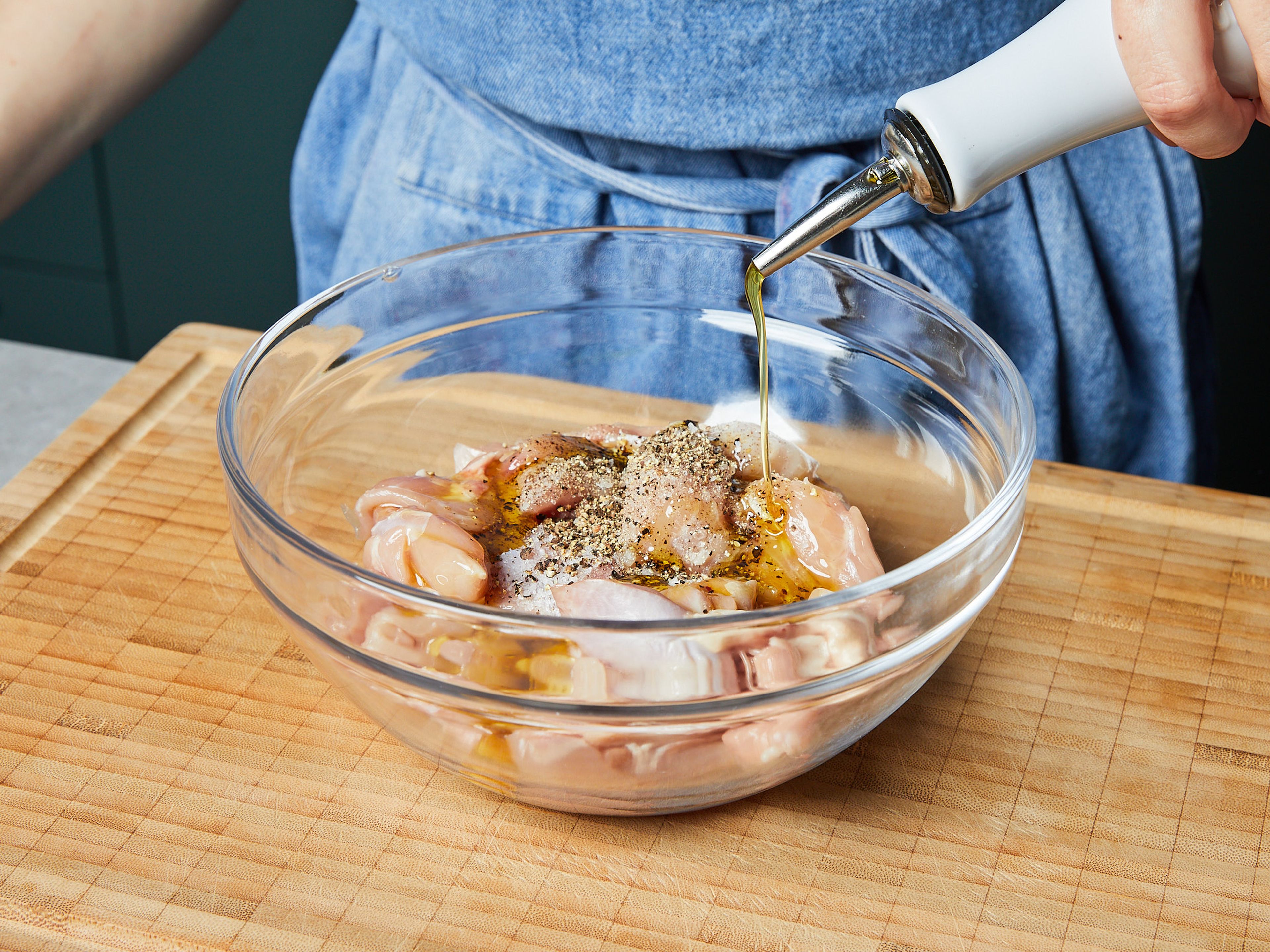 Das Hähnchenfleisch in grobe Stücke schneiden. In einer großen Schüssel mit Salz, Pfeffer und der Hälfte des Öls einreiben und ca. 5 Min. beiseitestellen und marinieren lassen. In der Zwischenzeit die Paprika entkernen. Paprika und Zwiebel fein würfeln. Knoblauch reiben. Petersilie fein hacken und zum Garnieren beiseitestellen.