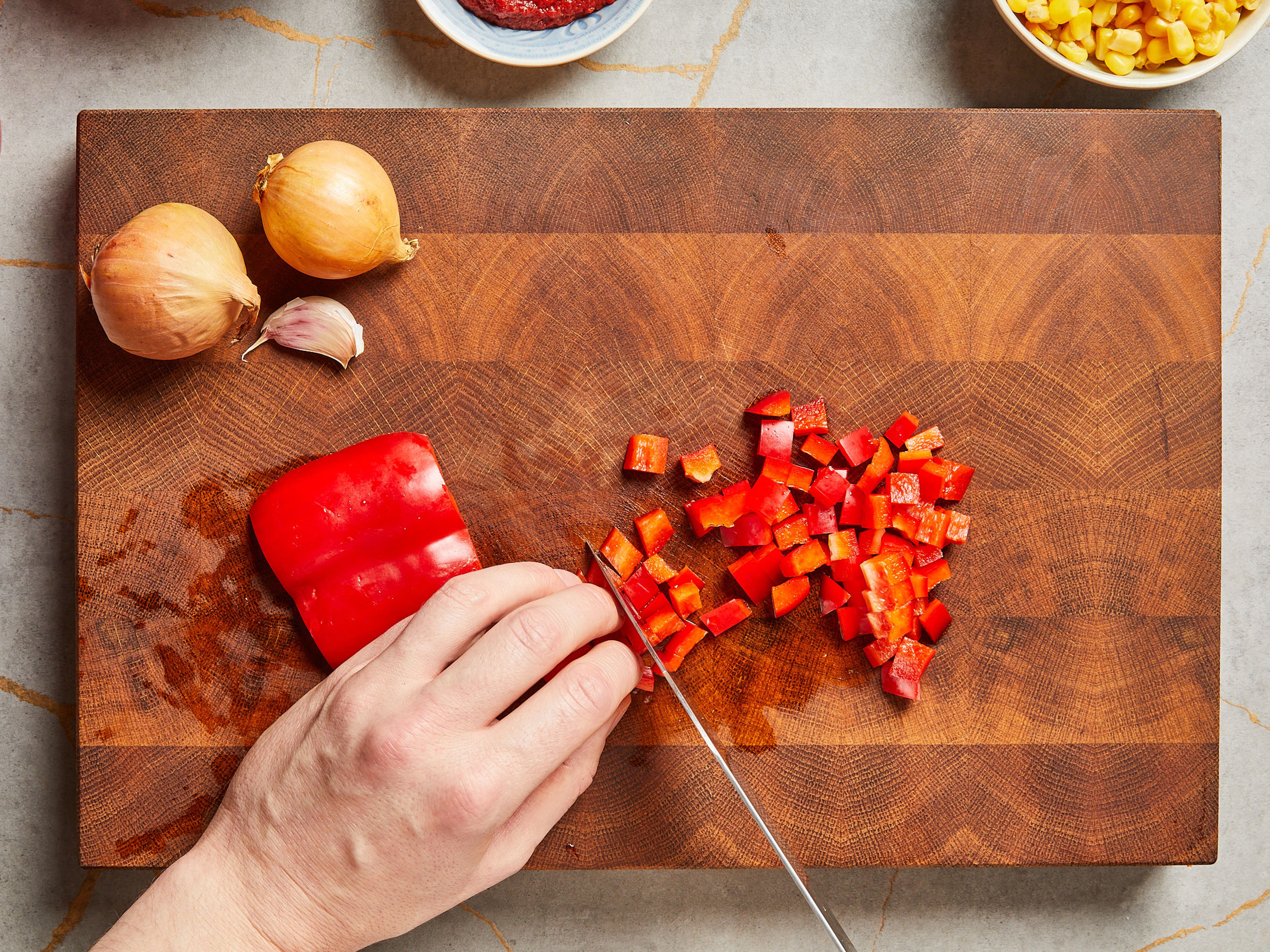 Zwiebel und Knoblauch schälen und fein hacken. Die rote Paprika in Würfel schneiden. Chilischote halbieren, entkernen und fein hacken.