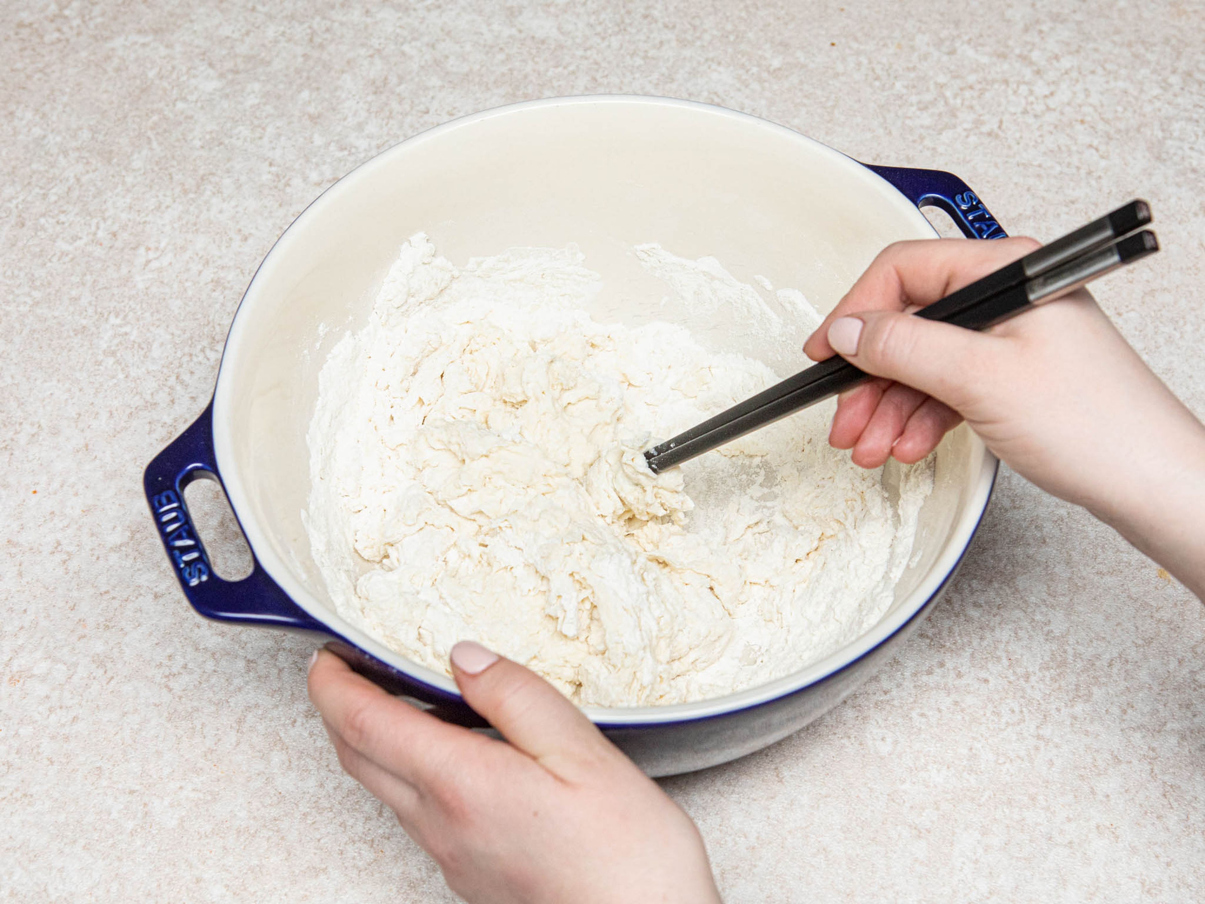 Mehl und Salz in einer großen Schüssel miteinader vermengen. Restliches Wasser langsam mit Stäbchen oder einem Holzlöffel einrühren, dann mit den Händen kneten, bis ein glatter Teig entstanden ist. Mit einem Geschirrtuch abdecken und für ca. 20 Min. ruhen lassen.