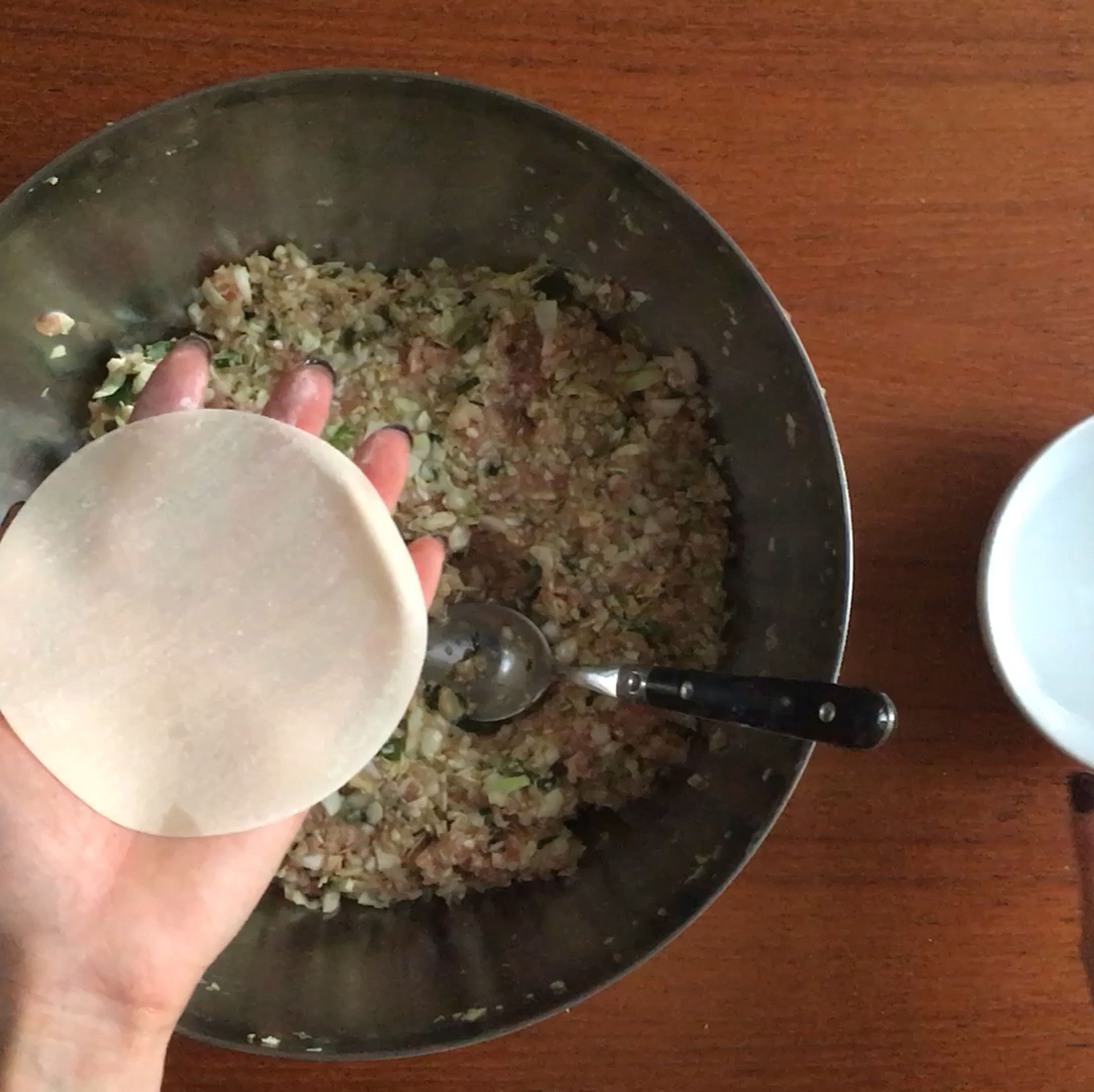 Have a small bowl ready, filled with water, for dipping your fingers. Take a gyoza wrapper and place it in the palm of your hand. Dip your finger in the bowl of water, and wet the edge of the gyoza wrapper. Use a spoon and take a small amount of filling and place it in the middle of the wrapper.