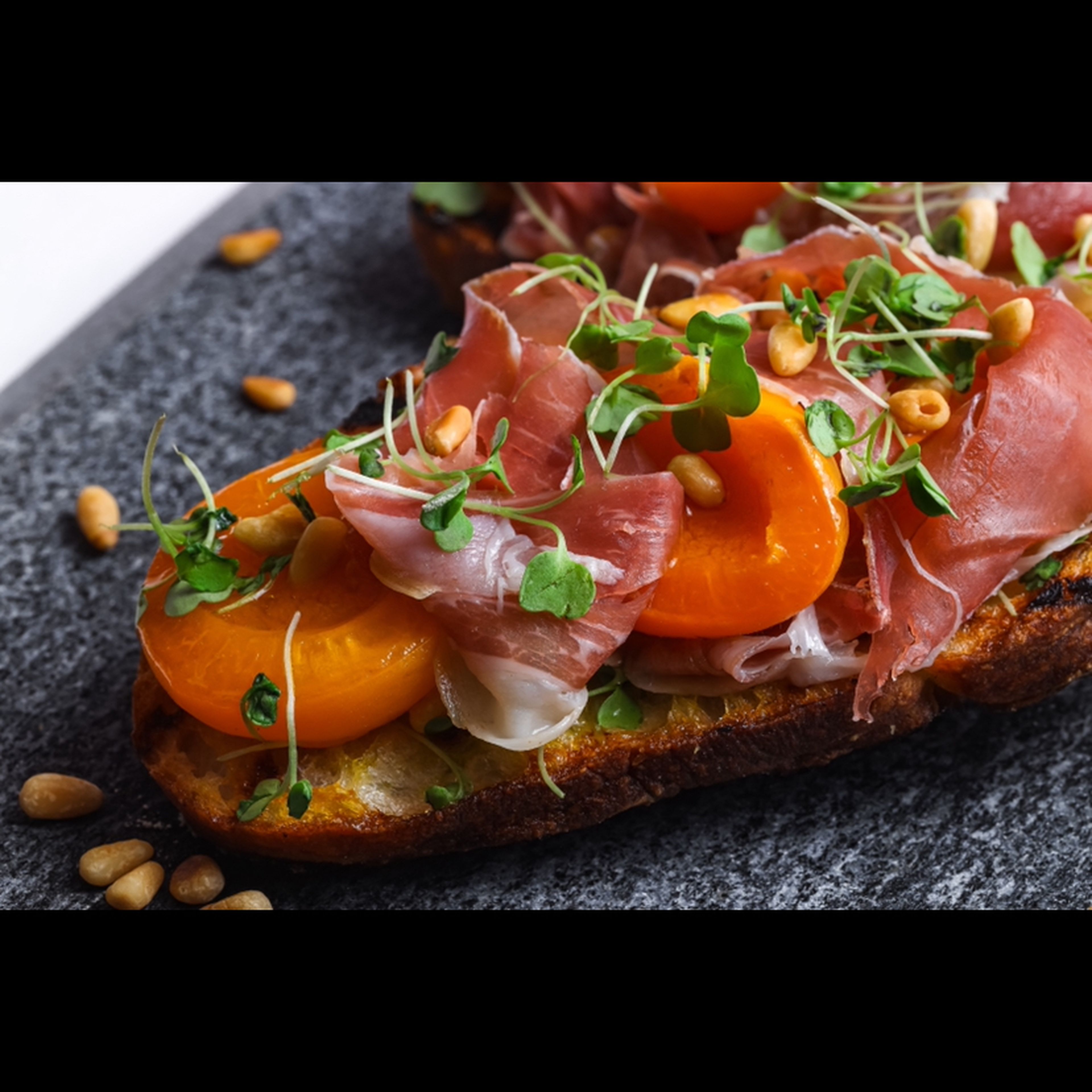 Layer prosciutto and cooked apricots onto grilled bread. Sprinkle on toasted pine nuts and micro arugula. Finish with a drizzle of olive oil.