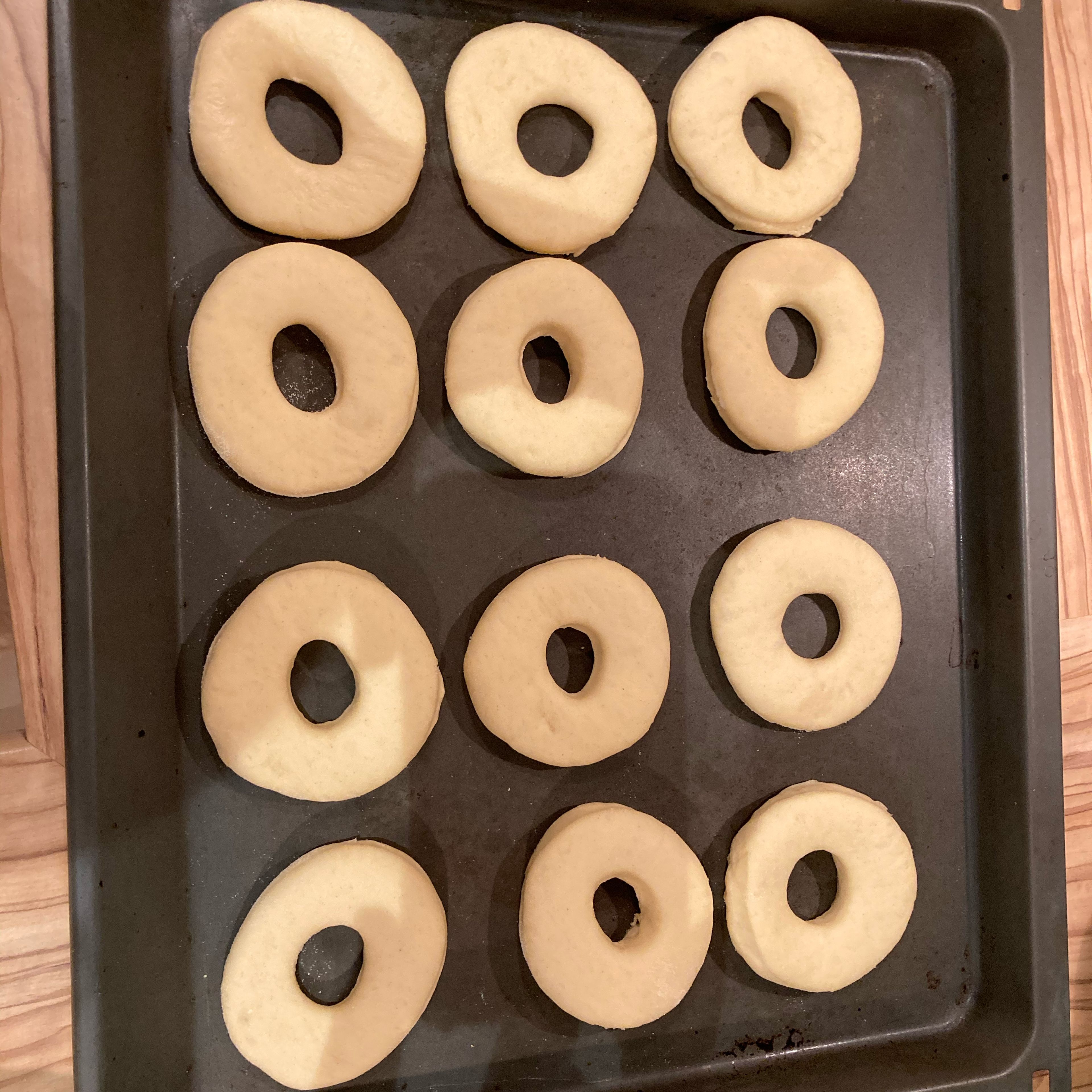 Nun den Teig für 45 Minuten ruhen lassen. Danach den Teig 1 cm dick ausrollen und mit einer runden, 8 cm Durchmesser Ausstechform ausstechen. Mit einer 2 cm Ausstechform mittig ausstechen, damit die typische Donutform entsteht. Die Teiglinge nochmal für 30-45 Minuten ruhen lassen.