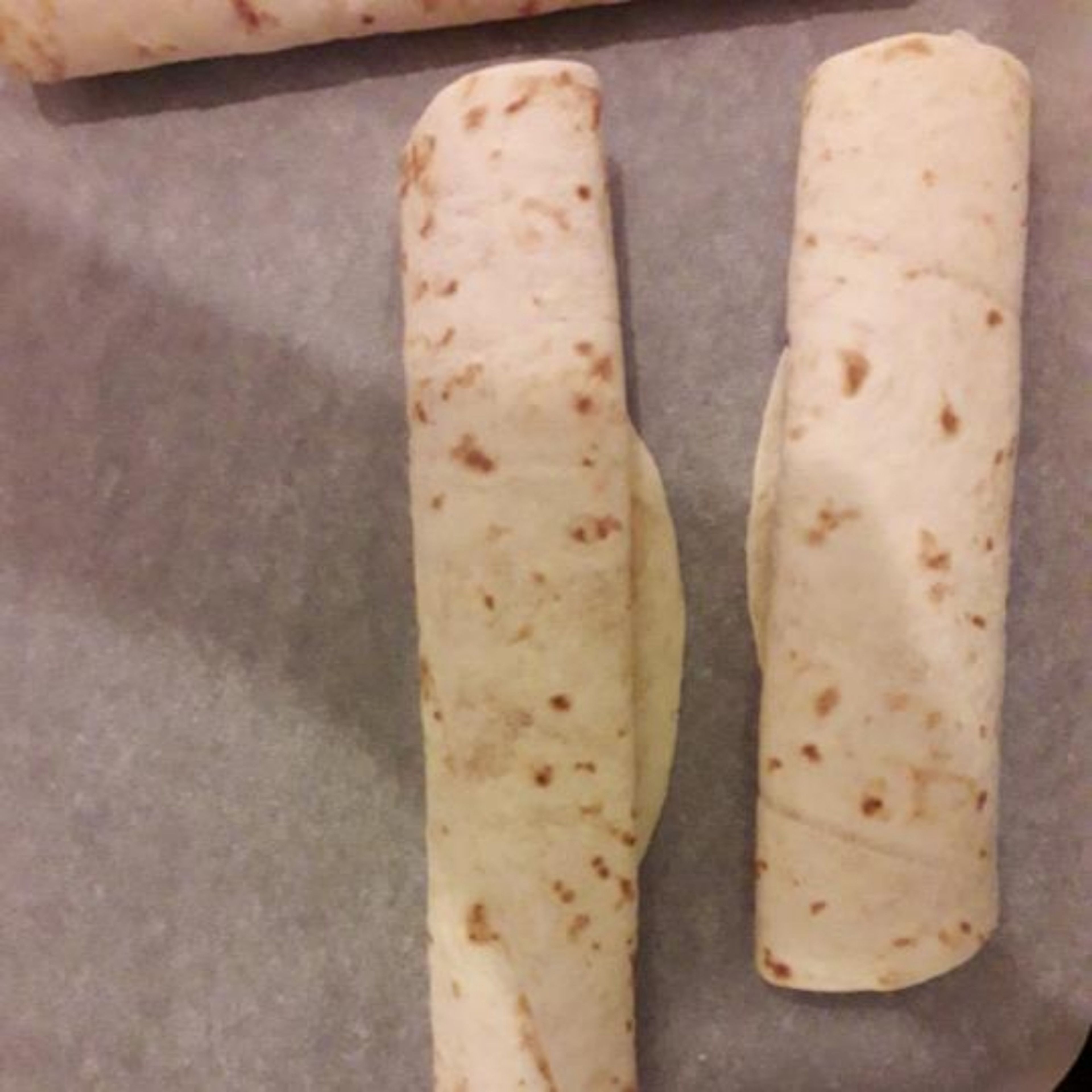 Once you put all your toppings on the tortilla, carefully role it and after it, lightly press it so it doesn't unroll on the tray. Wait until the oven is ready and them put them in.