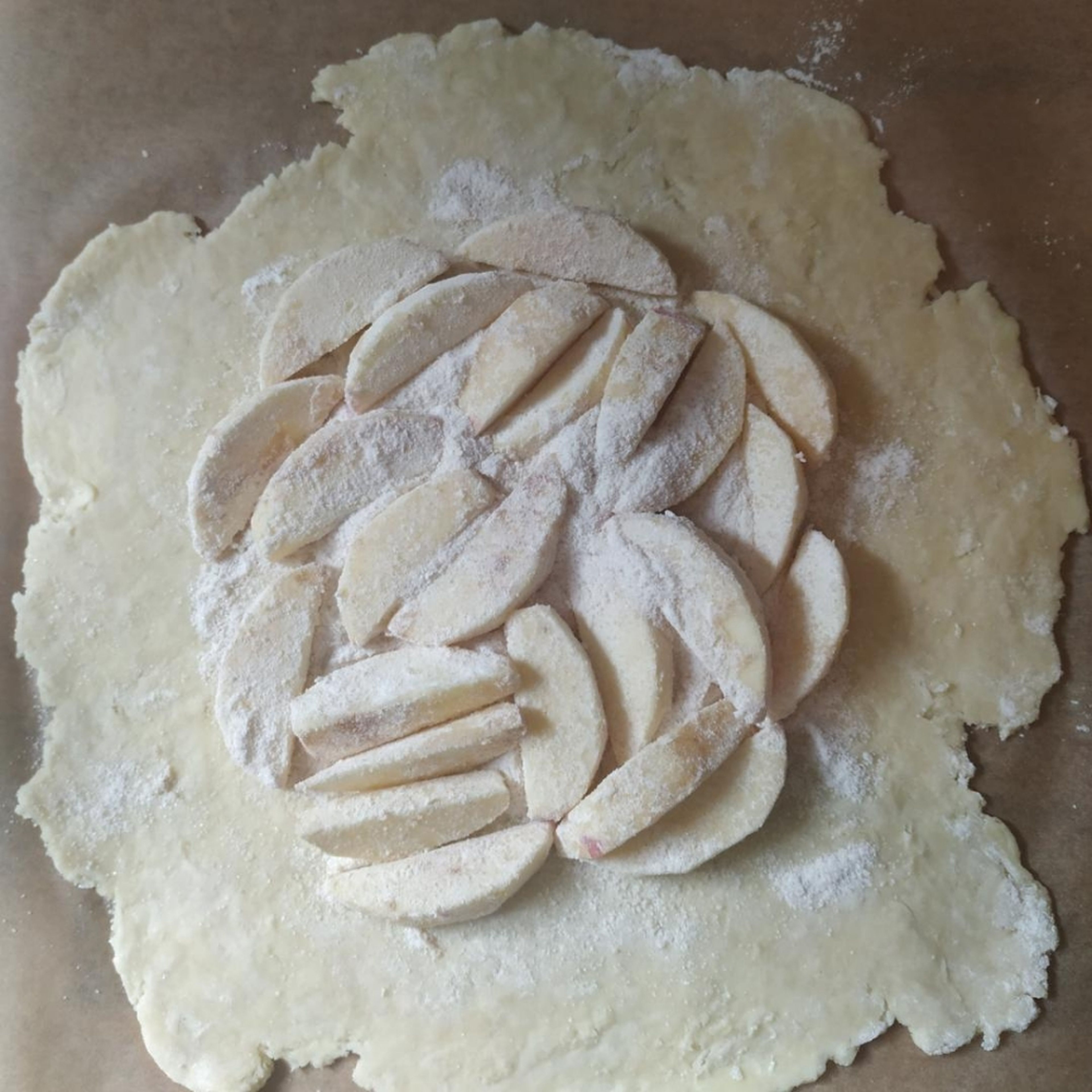 Den ausgerollten Teig auf ein Backblech mit Backpapier legen. Äpfel mittig verteilen, sodass noch ca 2 cm Platz zum Rand ist. Auch die übrige Mehl-Zucker-Mischung, die nicht an den Äpfeln haftet, verteilen, damit der Saft der Äpfel beim backen nicht den Boden durchweicht.
