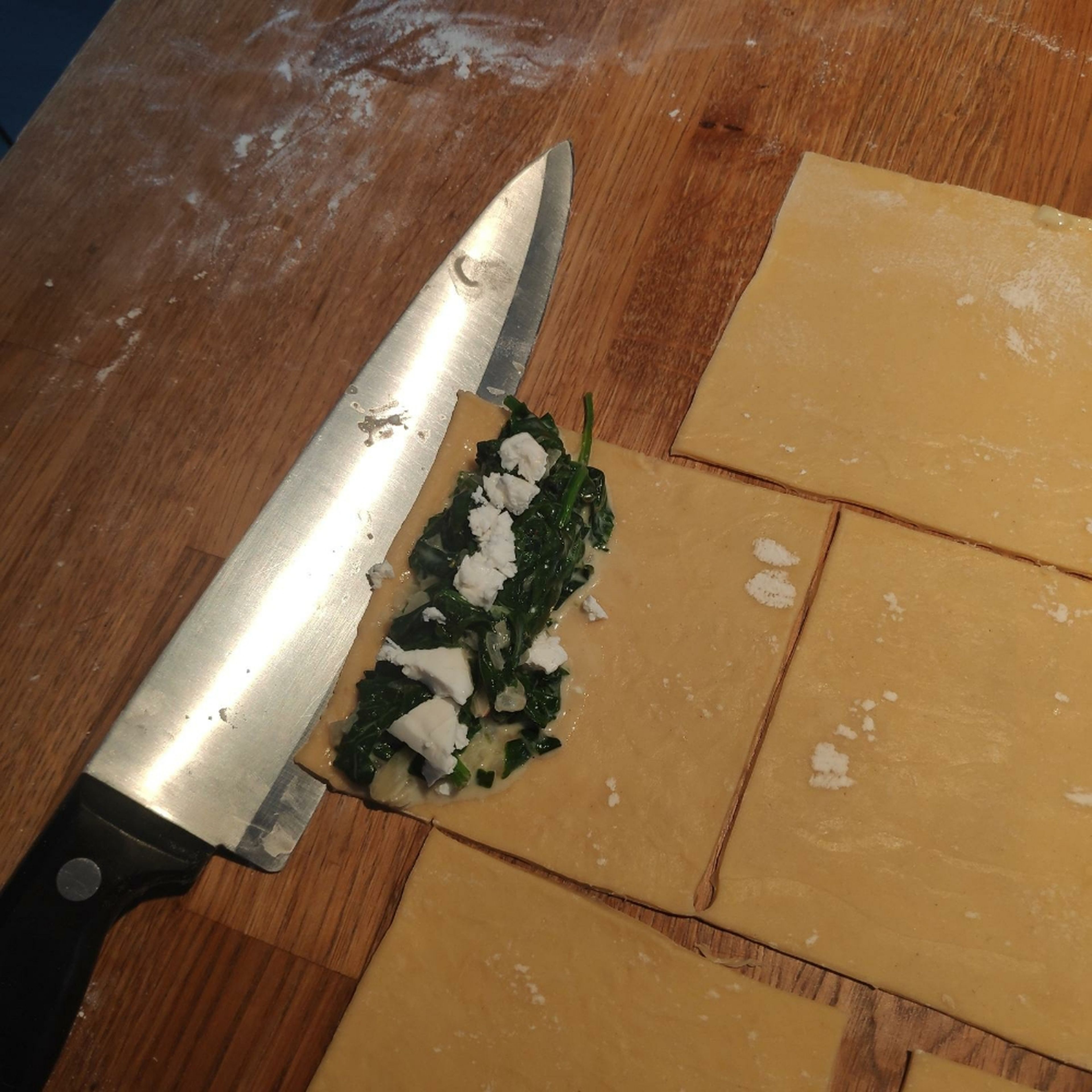 Etwas von der Spinatmasse zusammen mit zerkrümeltem Feta auf ein Teig-Quadrat geben.