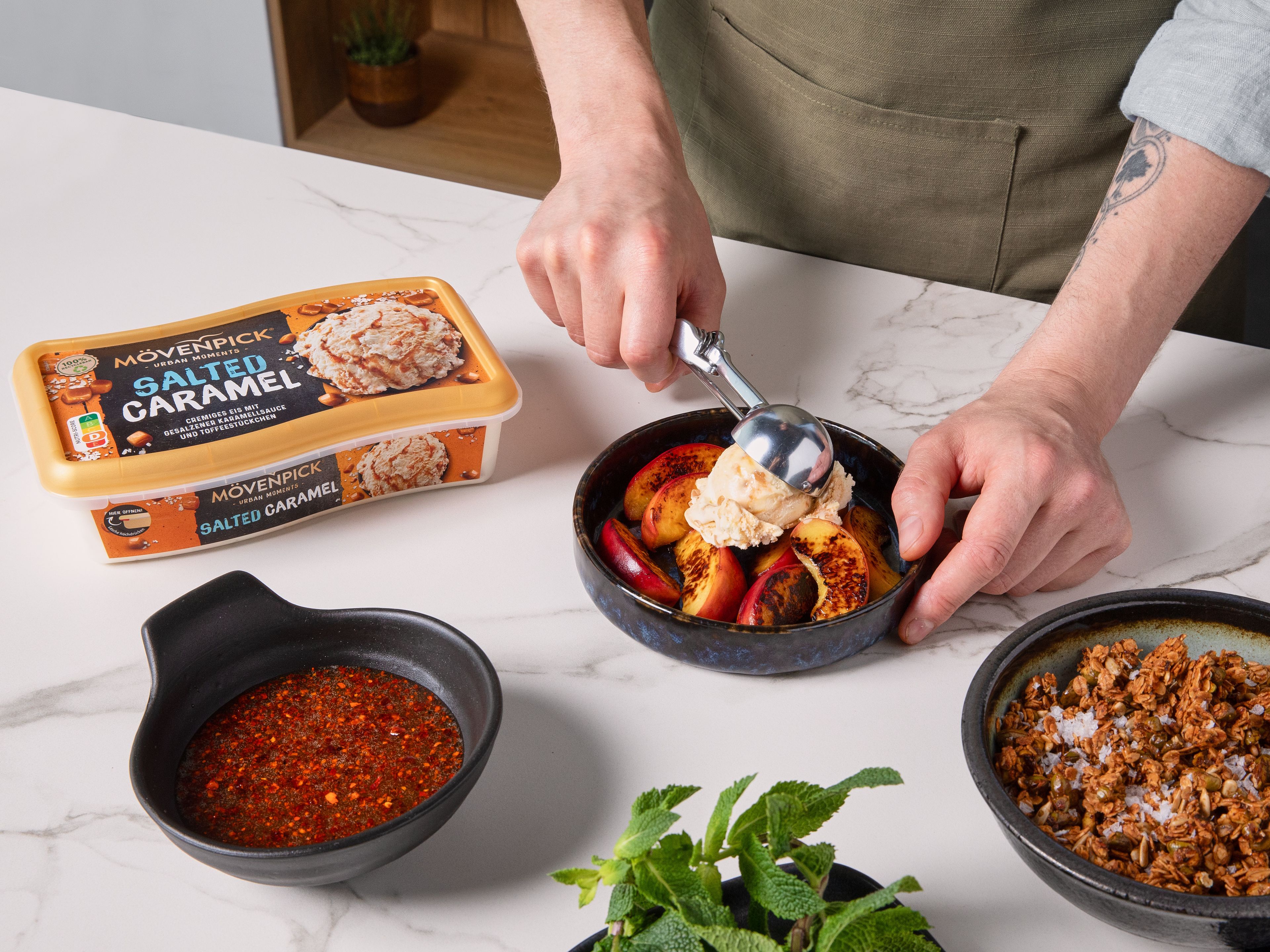 Gegrillte Pfirsiche auf einem Teller anrichten. Jeweils zwei Kugeln Mövenpick Salted Caramel Eis darauf geben, mit dem Chili-Pistazien-Granola bestreuen und mit frischer Minze garnieren. Nach Belieben mit dem restlichen Chili-Honig beträufeln.