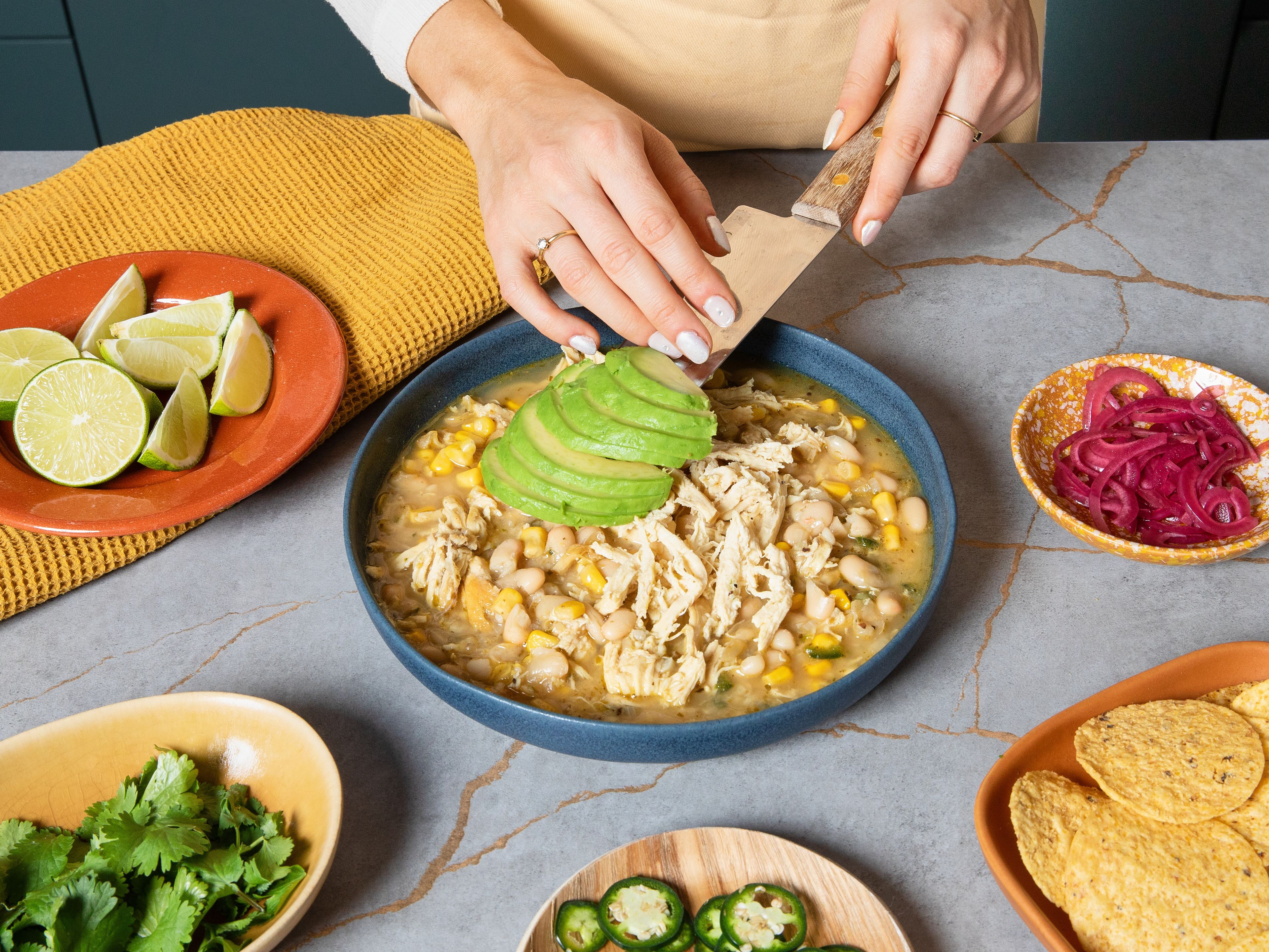 Stir in half of the sour cream and lime juice and season with salt and pepper to taste. Top with the remaining sour cream, avocado, fresh cilantro, and pickled onions, if desired. Serve with lime wedges and tortilla chips.