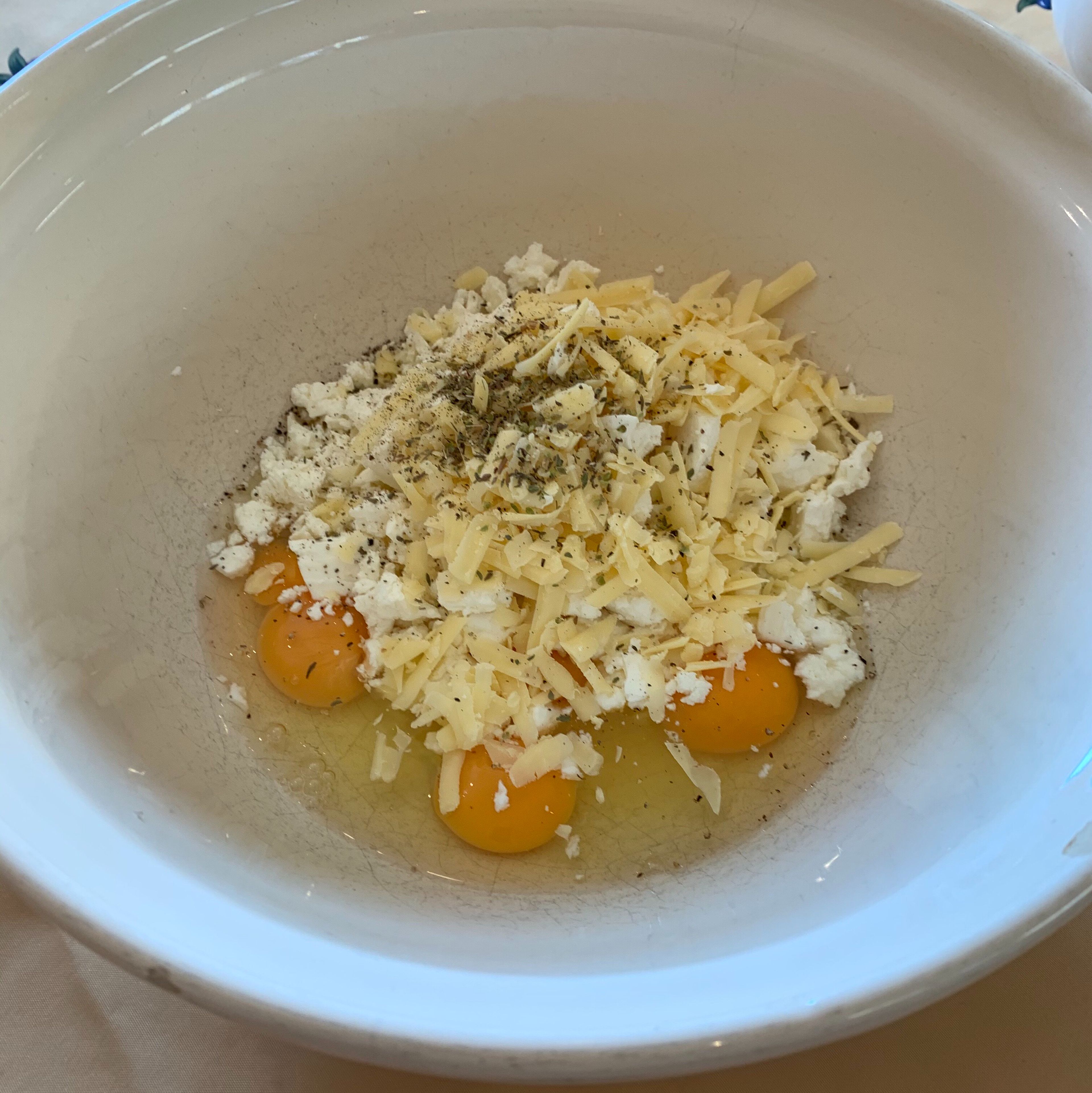 Crack the eggs into a large mixing bowl and crumble the feta . Grate the cheddar, then add the oregano and pepper