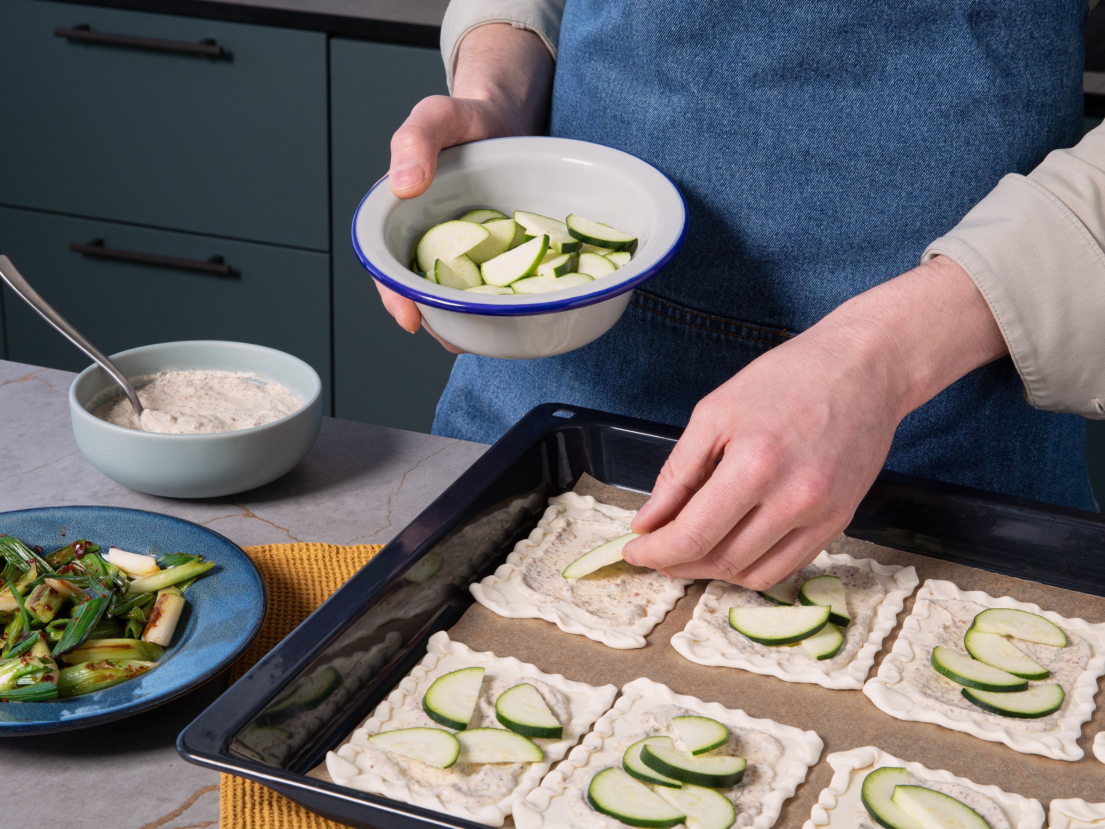 Blätterteig ausbreiten und in 8 Rechtecke schneiden. Die Ränder jedes Rechtecks ca. 1 cm umklappen und festdrücken. Die Hälfte der Frischhain Natur Mischung auf den Teigstücken verteilen. Mit Zucchini und Frühlingszwiebeln belegen und im vorgeheizten Ofen für ca. 15 Min. backen.