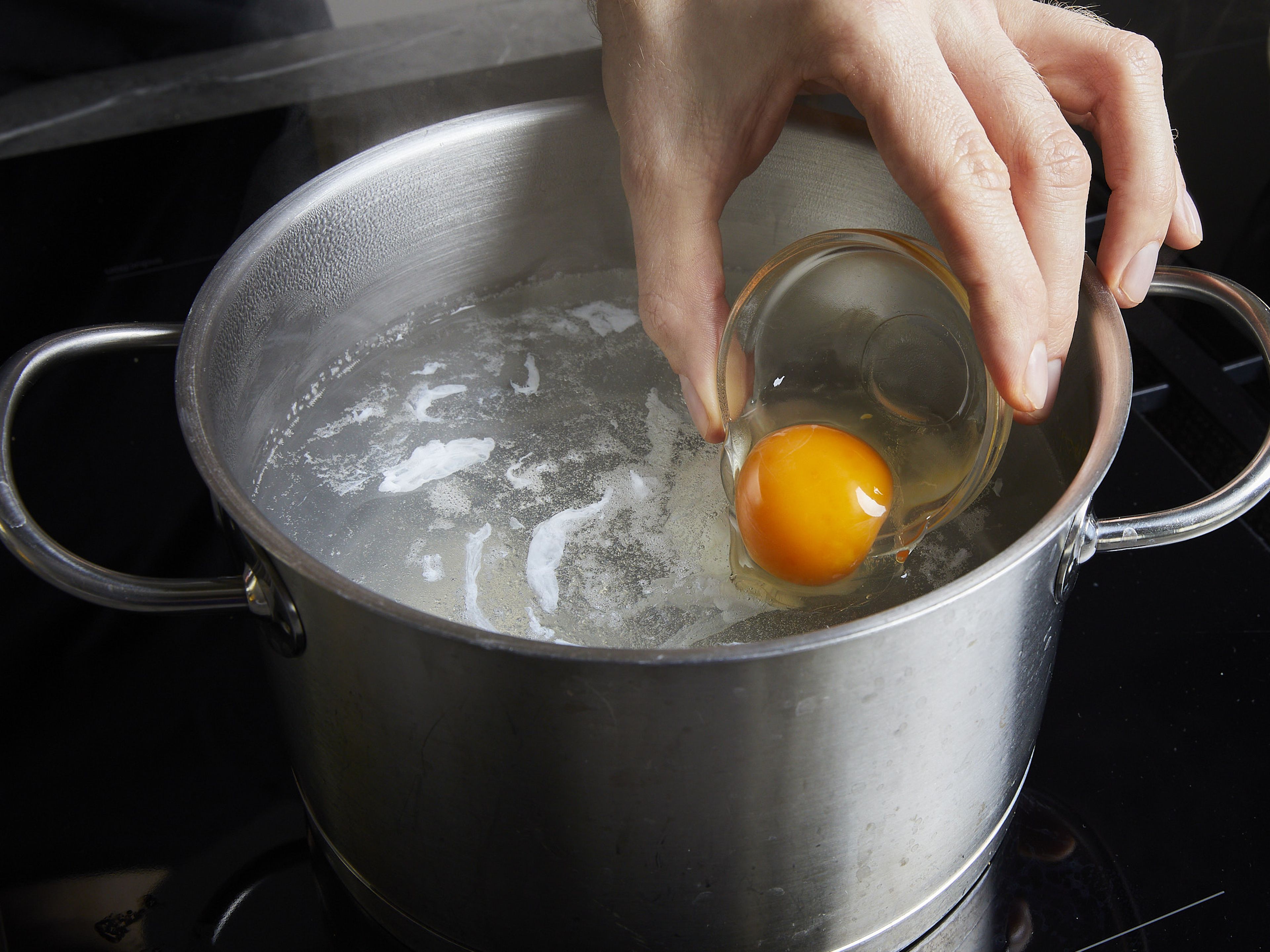 Um die Eier für die Eggs Benedict zu pochieren, einen mittelgroßen Topf mit Wasser füllen und dieses zum Sieden (nicht Kochen!) bringen. Jedes Ei einzeln vorsichtig in ein feinmaschiges Sieb schlagen, um den wässrigen Teil des Eiweißes zu entfernen, und dann vorsichtig in eine kleine Schüssel geben. Jedes Ei einzeln in den Topf geben und das Wasser mit einem Löffel umrühren, um einen Strudel zu erzeugen. Die Eier ca. 3–4 Min. kochen, bis das Eiweiß fest ist, dann mit einem Schaumlöffel oder einem Sieb herausnehmen. Diesen Schritt mit den restlichen Eiern wiederholen.