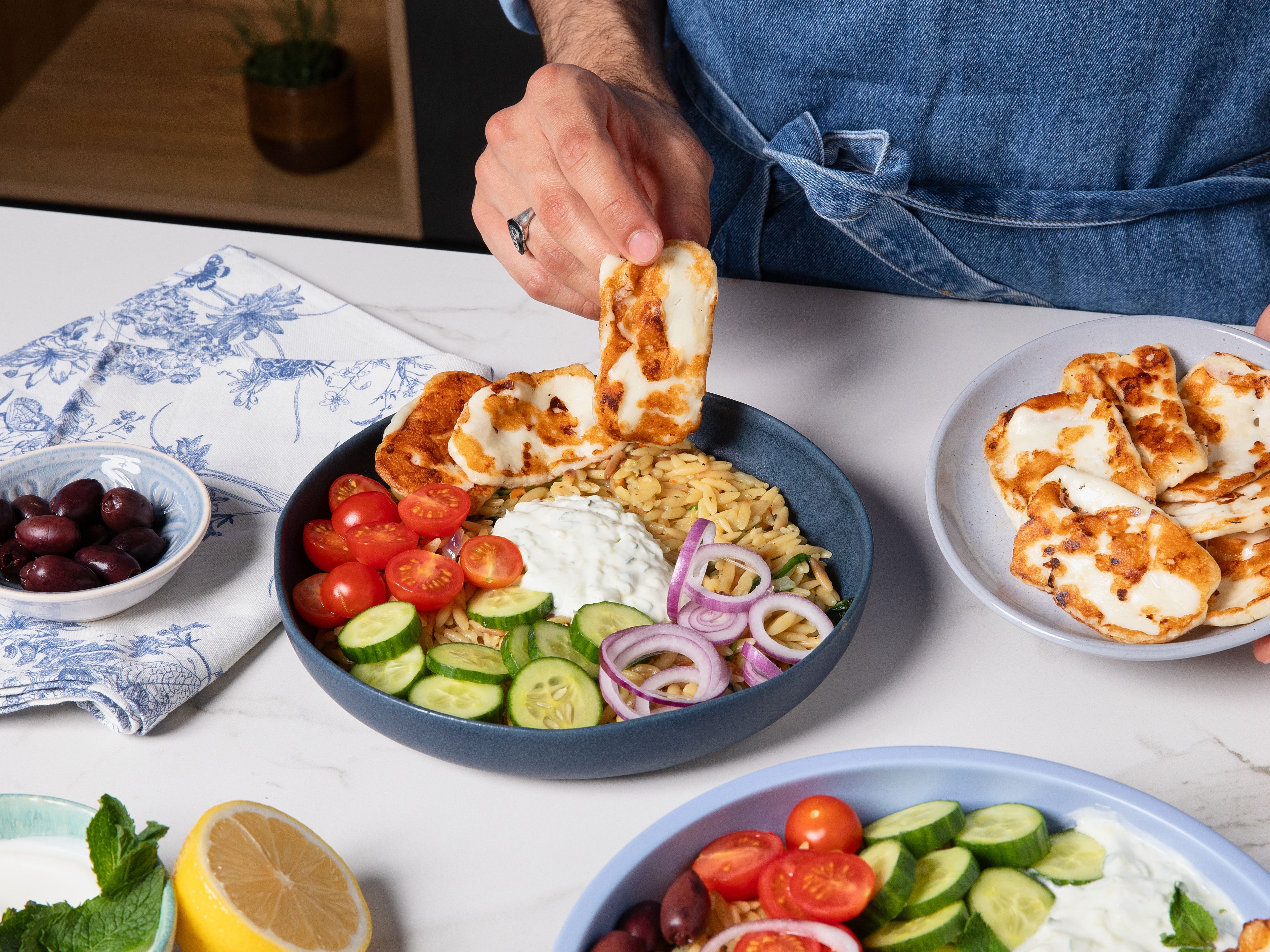 Once the orzo cooled down, assemble the bowls. To a deep bowl add orzo, tomatoes, cucumber, red onion, olives, tzatziki, and halloumi. Sprinkle salt, pepper, and lemon juice. Serve with mint leaves on top.