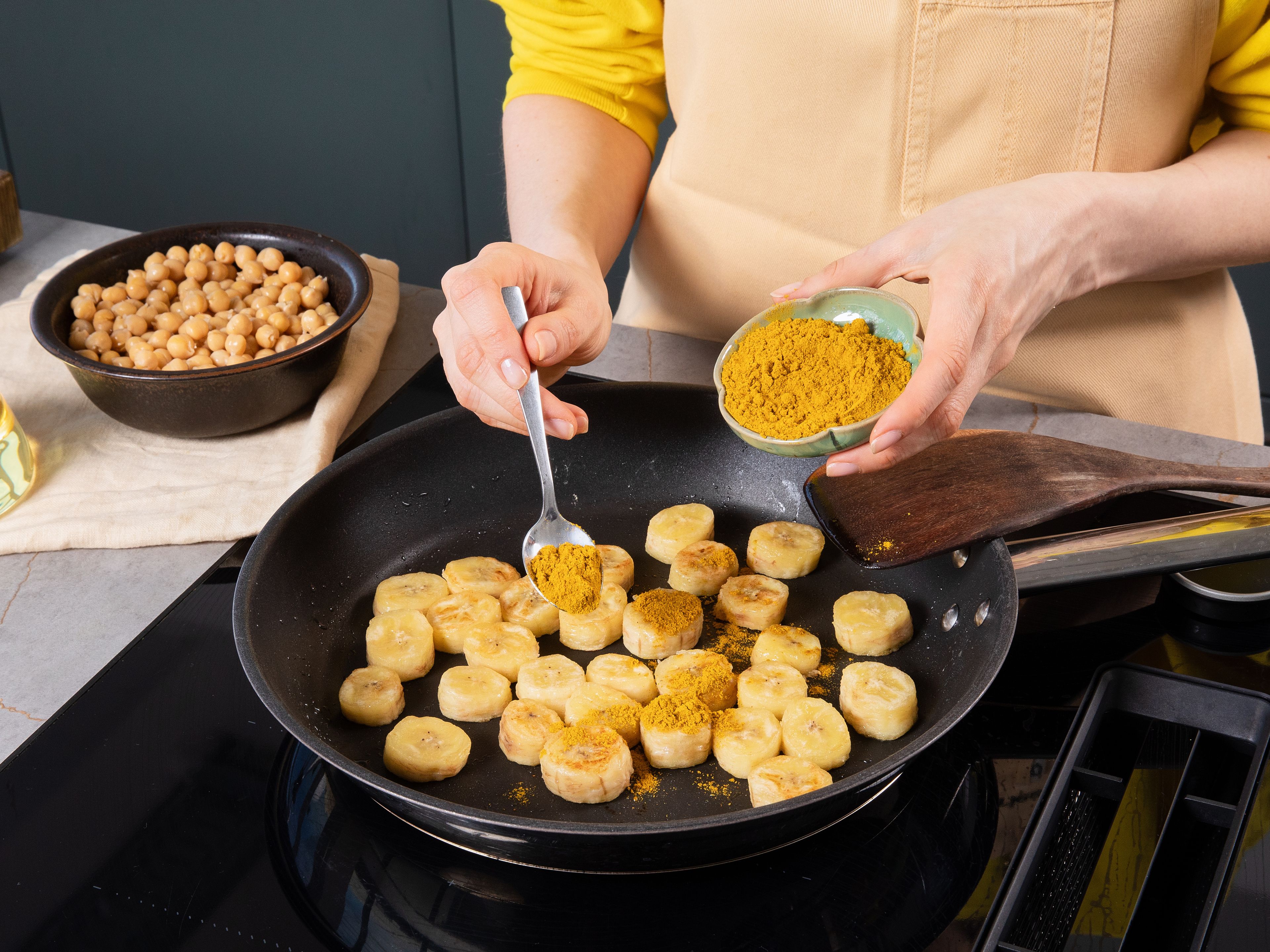 Zwiebel, Knoblauch und Ingwer schälen. Knoblauch und Ingwer fein hacken oder reiben, Zwiebel fein würfeln. Bananen in ca. 1,5–2 cm dicke Scheiben schneiden. Kichererbsen abtropfen lassen. Öl in einer großen Pfanne bei mittlerer bis hoher Hitze erhitzen. Bananenscheiben ca. 2–3 Min. pro Seite goldbraun anbraten, bis sie sich leicht lösen. Hitze leicht reduzieren, die Hälfte des Currypulvers über die Bananen streuen und ca. 20–30 Sek. schwenken, bis es duftet. Mit Salz würzen, herausnehmen und beiseite stellen.