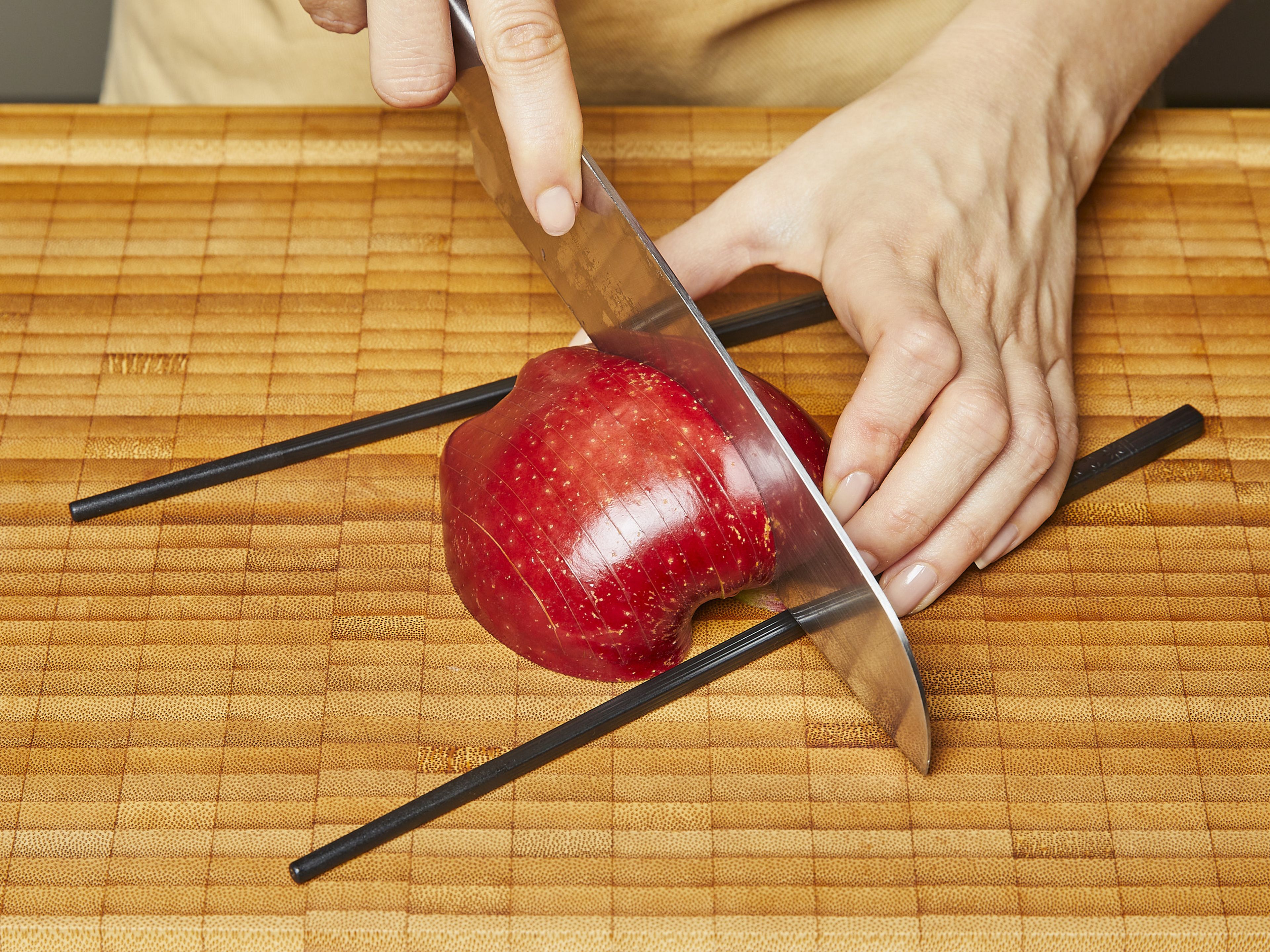 Äpfel halbieren und das Kerngehäuse vorsichtig herauslösen, dabei nicht zu tief einschneiden. Mit der Schnittfläche nach unten setzen und mit einem scharfen Messer jeweils alle ca. 0,3–0,5 cm einschneiden, dabei aber nicht ganz durchschneiden. Tipp: Dafür jeweils oben und unten ein Essstäbchen an den Apfel legen.