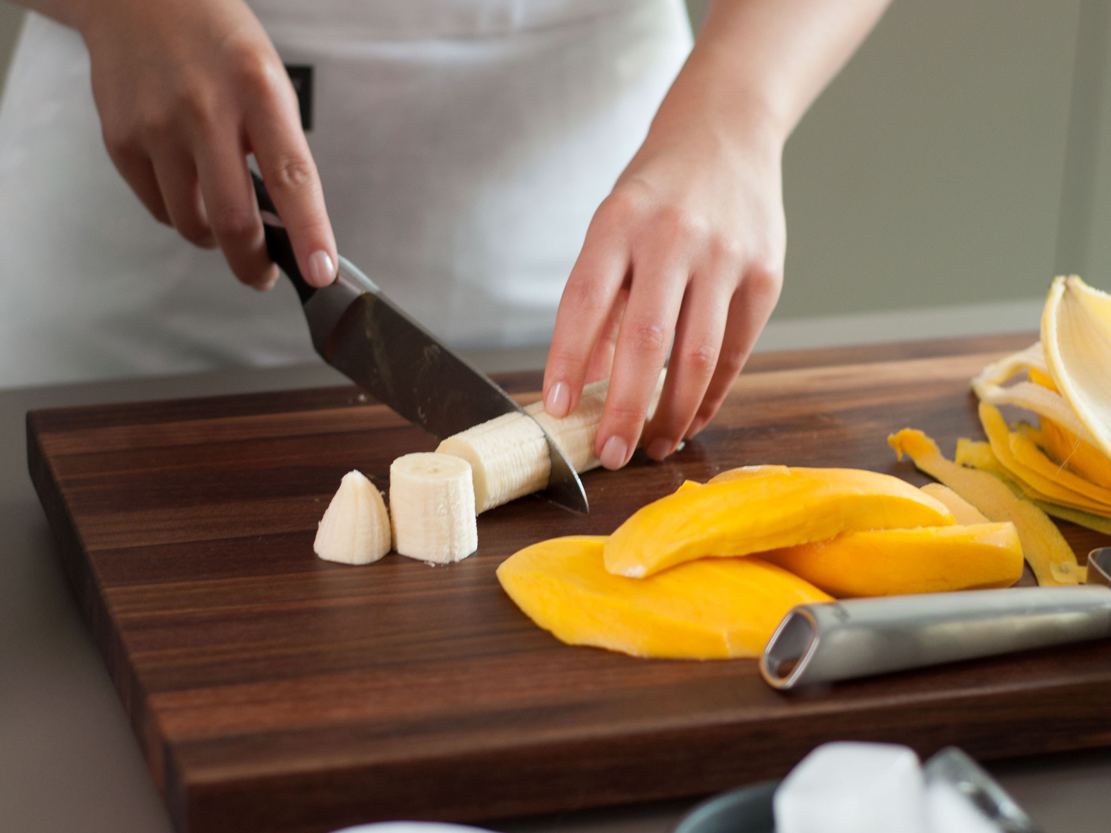 Banane schälen und in grobe Stücke schneiden. Mango schälen und Fruchtfleisch vom Kern schneiden.