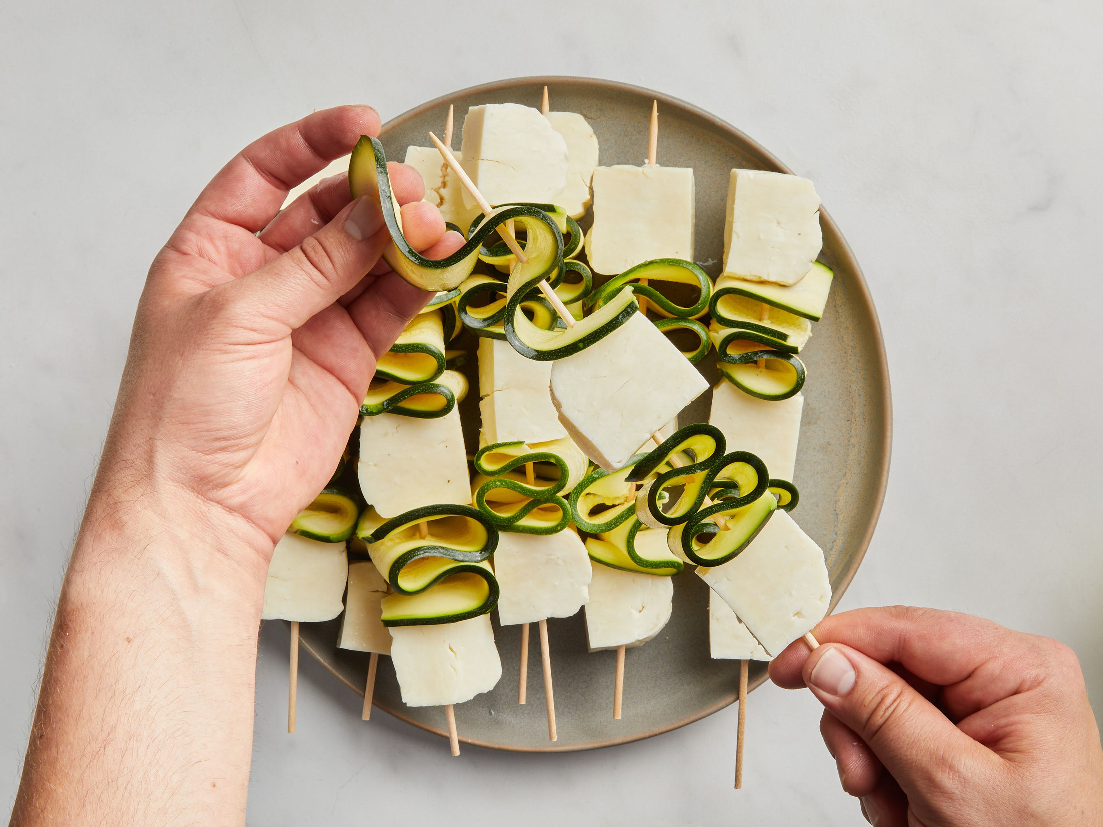 Now assemble the skewers. To do this, start and end each skewer with a halloumi cube and alternate the zucchini slices in an S-shape between them. There should be 3 halloumi cubes per skewer. Brush with olive oil and season with salt and pepper.