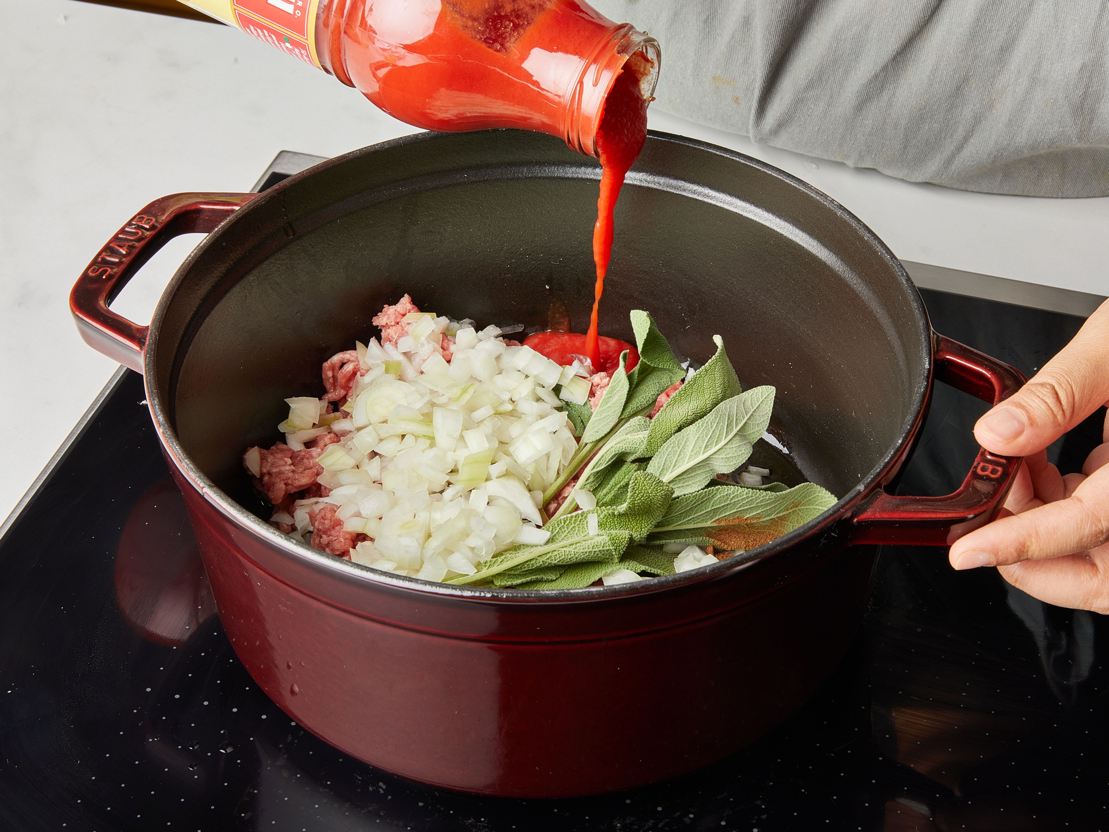 Beginne zuerst mit der Soße. Bedecke den Boden eines kalten (!) großen Topfes großzügig mit Olivenöl. Hackfleisch, Lorbeerblatt, Rosmarin, Thymian und Salbei hinzugeben, sowie Piment, falls du welchen verwendest. Zwiebel fein würfeln und ebenfalls dazugeben. Mit passierten Tomaten auffüllen und mit Salz und Pfeffer würzen. Dann den Topf auf den Herd stellen und zugedeckt bei mittlerer Hitze ca. 30 Min. köcheln lassen. Zwischendurch gelegentlich umrühren.