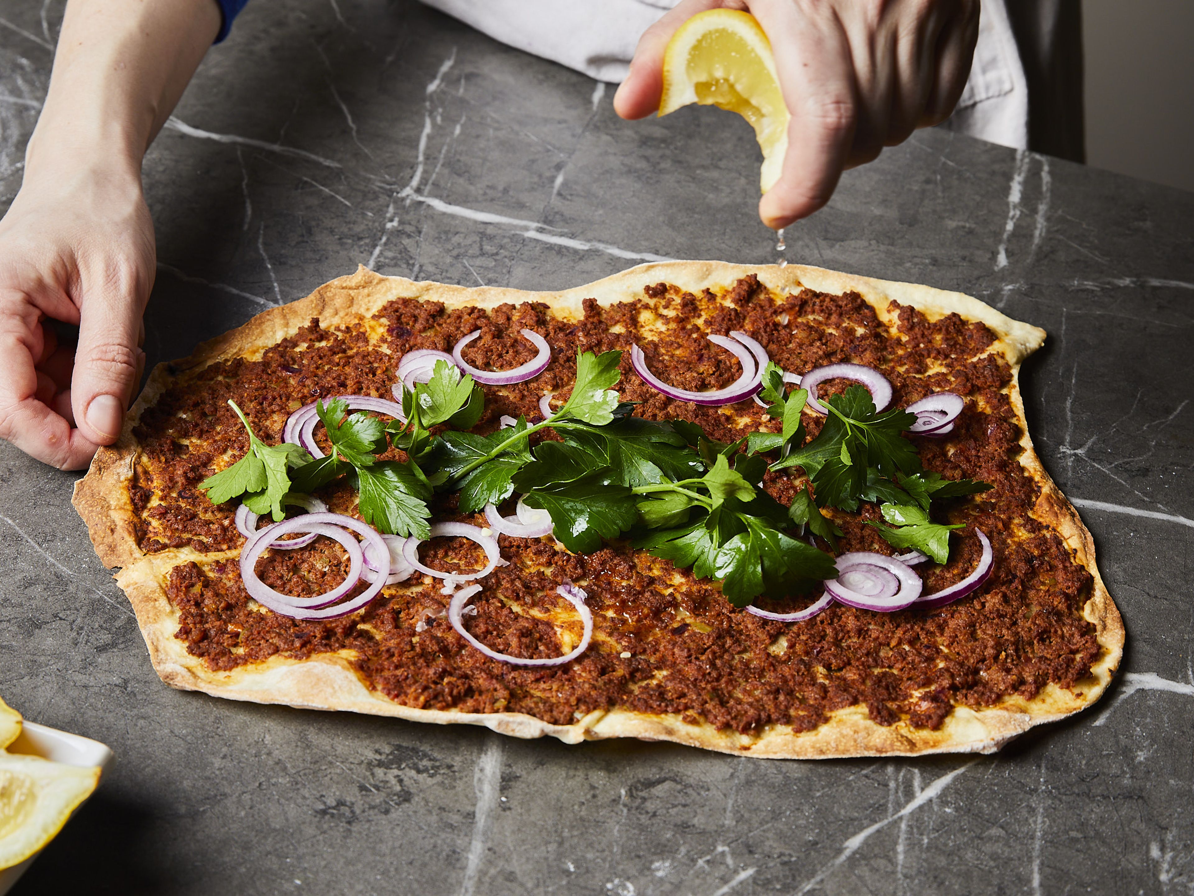 While the lahmacun is baking, pluck the parsley leaves and chop them roughly. Finely slice the remaining red onions. Cut the lemon into wedges. Remove the lahmacun from the oven and drizzle with a little lemon juice. Serve with the parsley and onions.