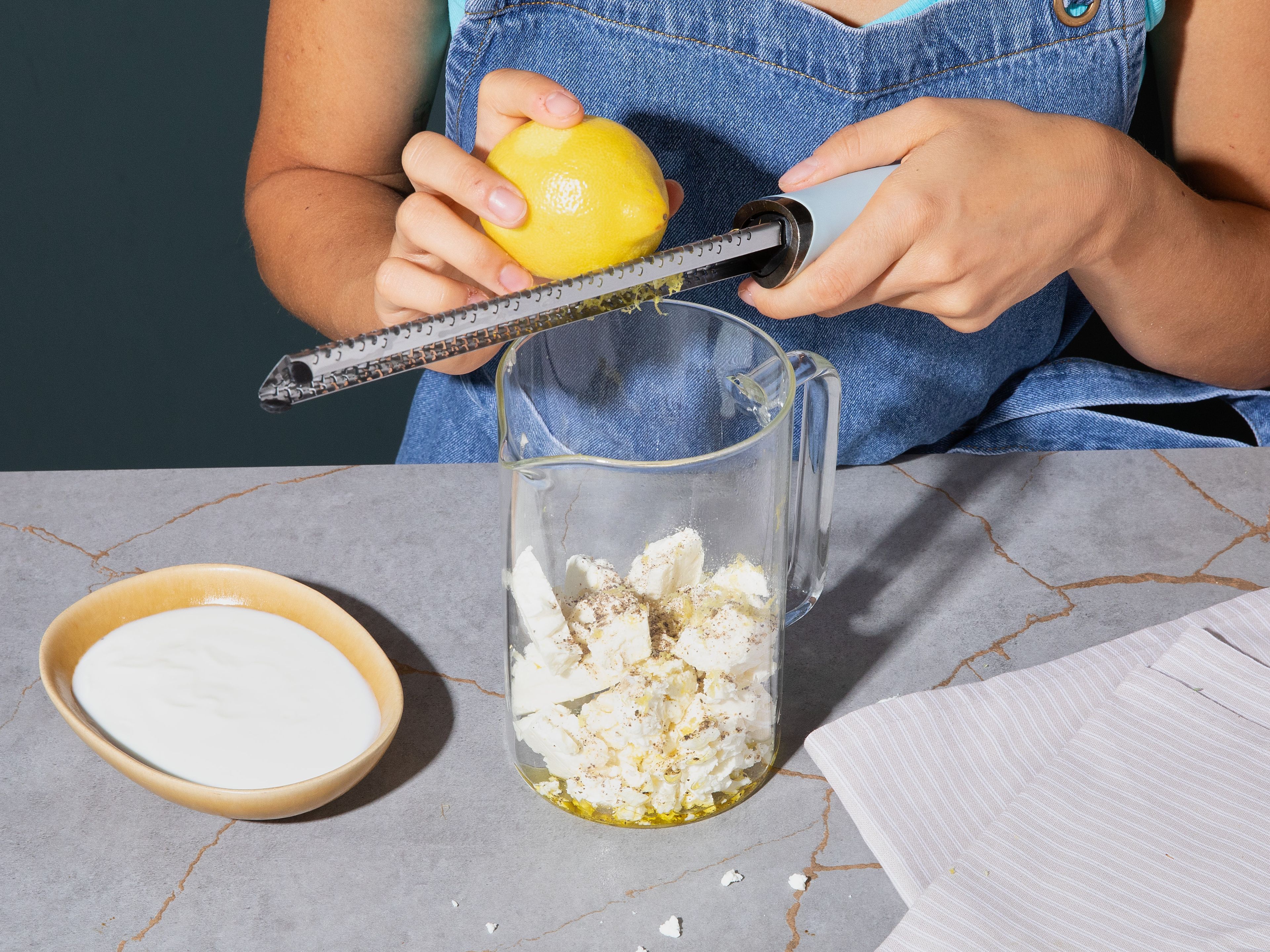 Coarsely crumble feta and place in a tall mixing container with yogurt. Grate lemon zest and add to container, season with pepper, and puree with an immersion blender into a smooth cream.