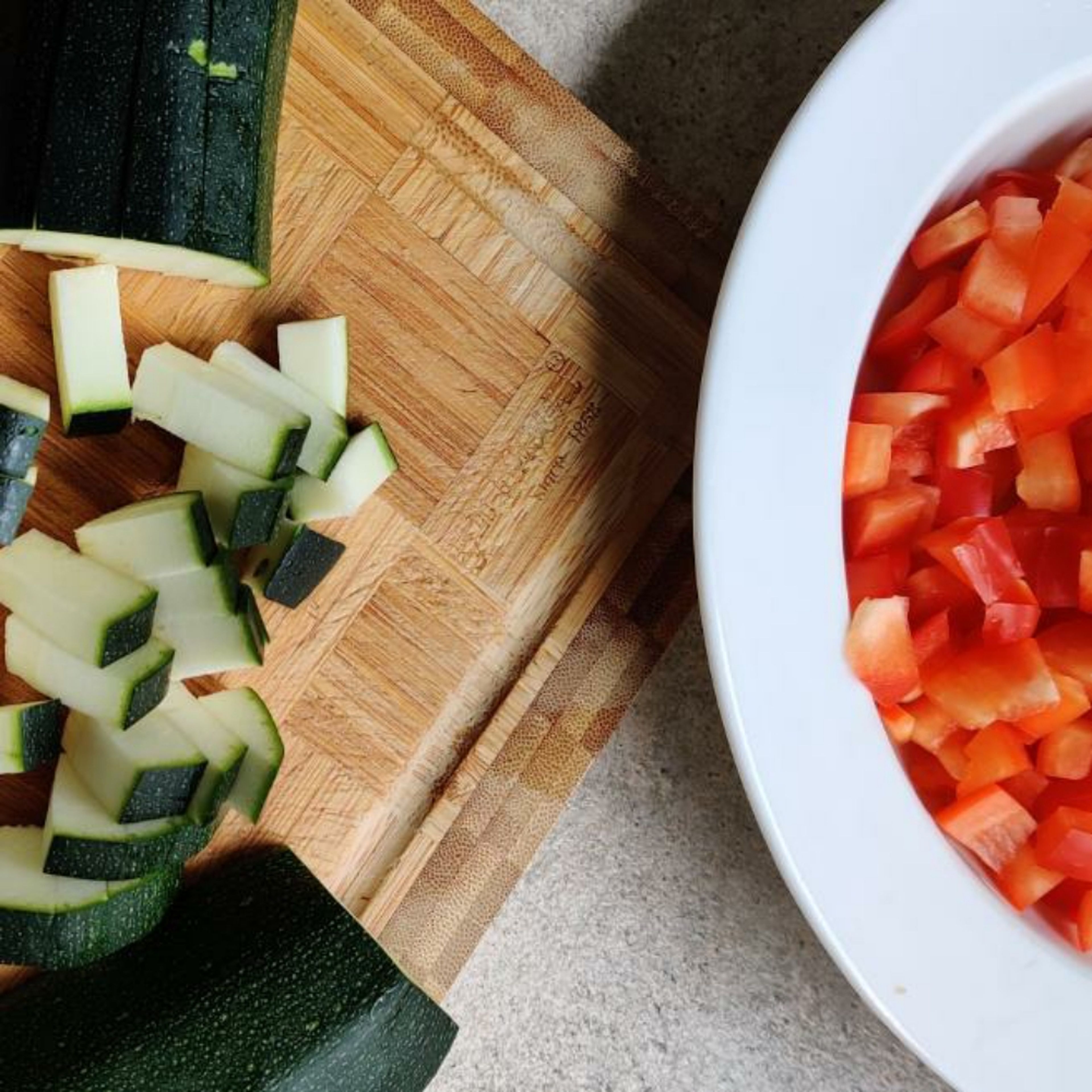 Paprika, Knoblauchzehen und Zucchini kleinschneiden und zusammen anbraten. Zusätzlich die Tomaten klein schneiden und bereitstellen.