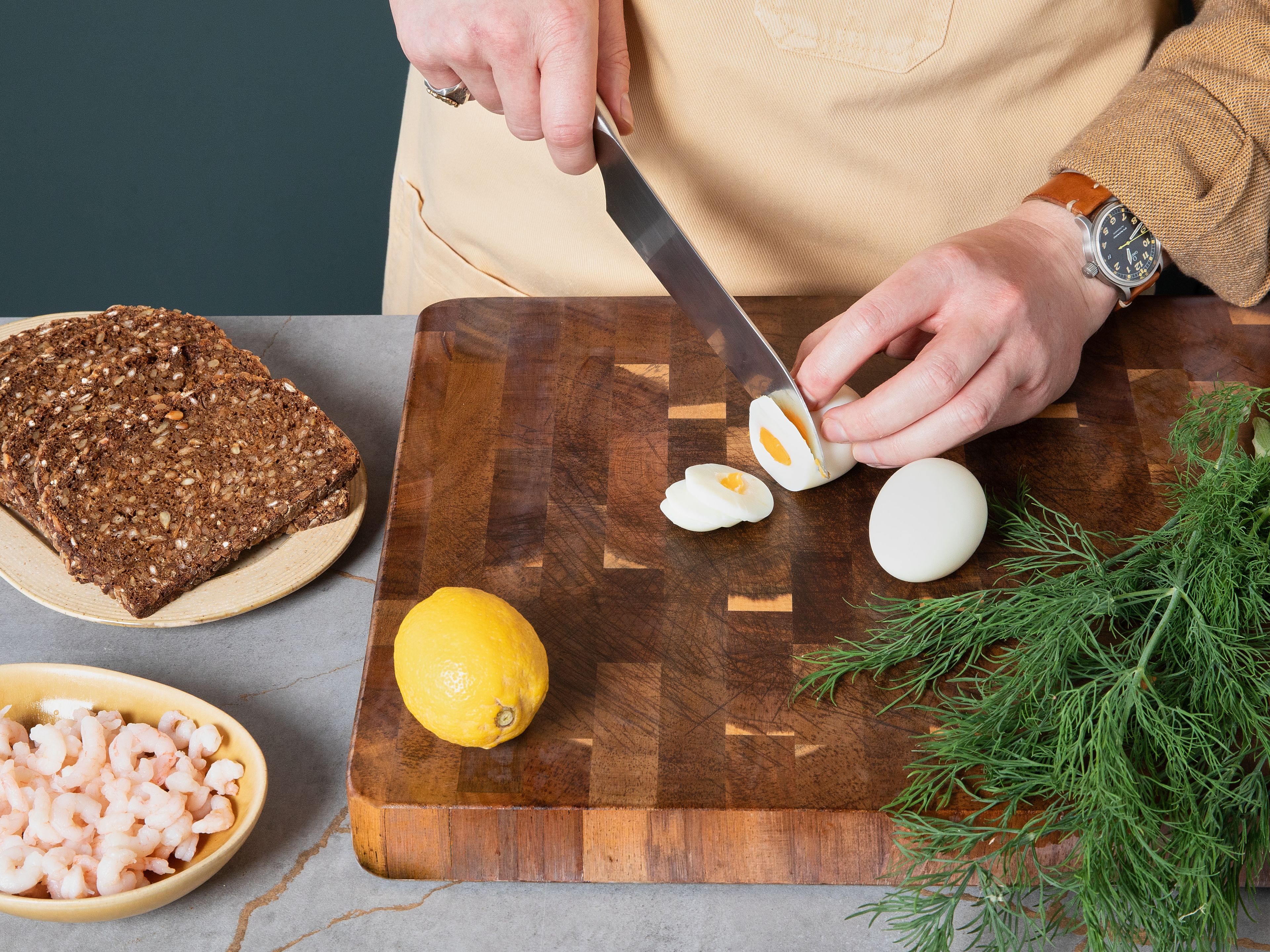 Für das Ei- und Garnelen-Smørrebrød: Einen kleinen Topf mit Wasser zum Kochen bringen und die Eier ca. 8 Min. kochen – ein Ei pro Scheibe Brot. In der Zwischenzeit die Brotscheiben großzügig mit Butter bestreichen. Sobald die Eier gekocht sind, pellen und in ca. 0,5 cm dicke Scheiben schneiden. Die Eierscheiben auf dem Brot verteilen, mit Salz und Pfeffer würzen und mit Mayonnaise beträufeln. Anschließend die Garnelen daraufgeben, großzügig mit Dill garnieren und mit einem Spritzer Zitrone verfeinern.